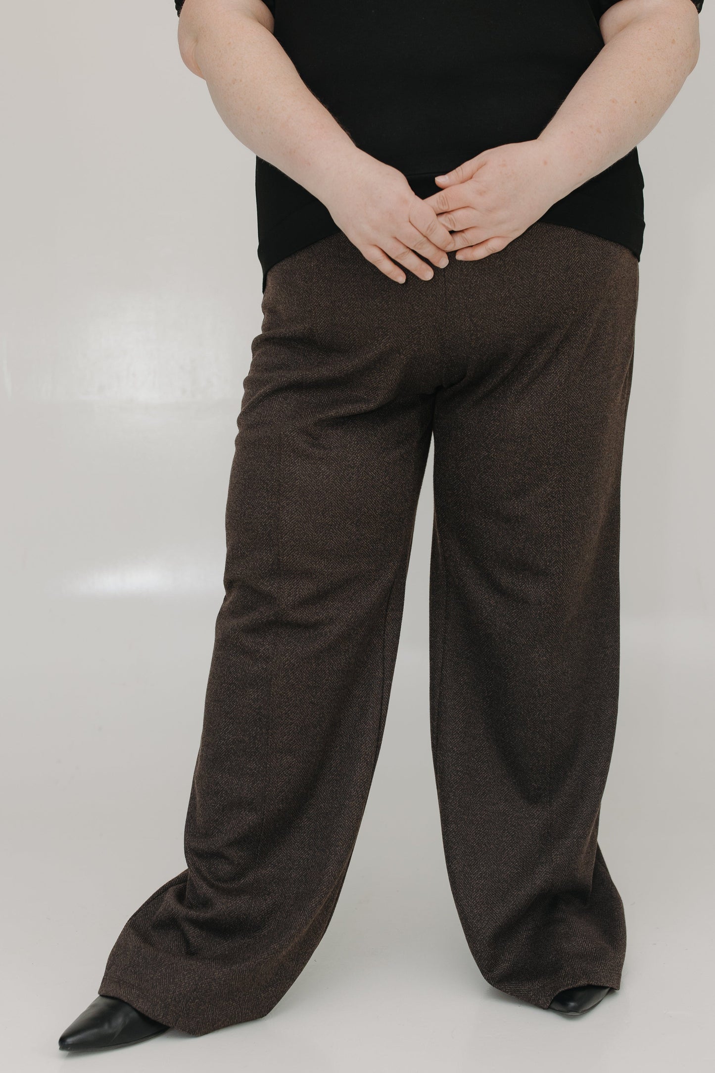 Person wearing brown wide-leg pants and a black top on a white background