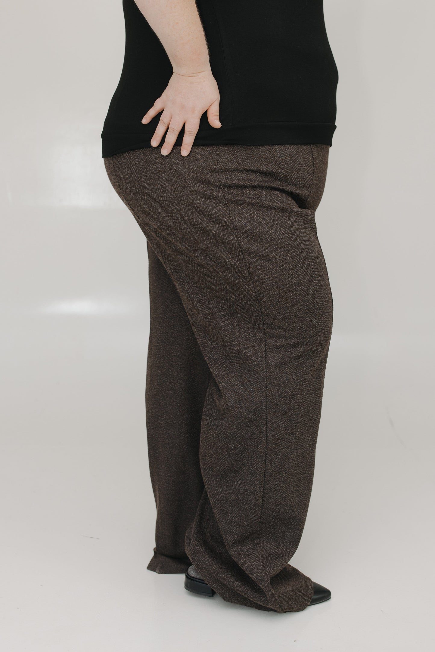 Person wearing brown pants and a black top on a white background
