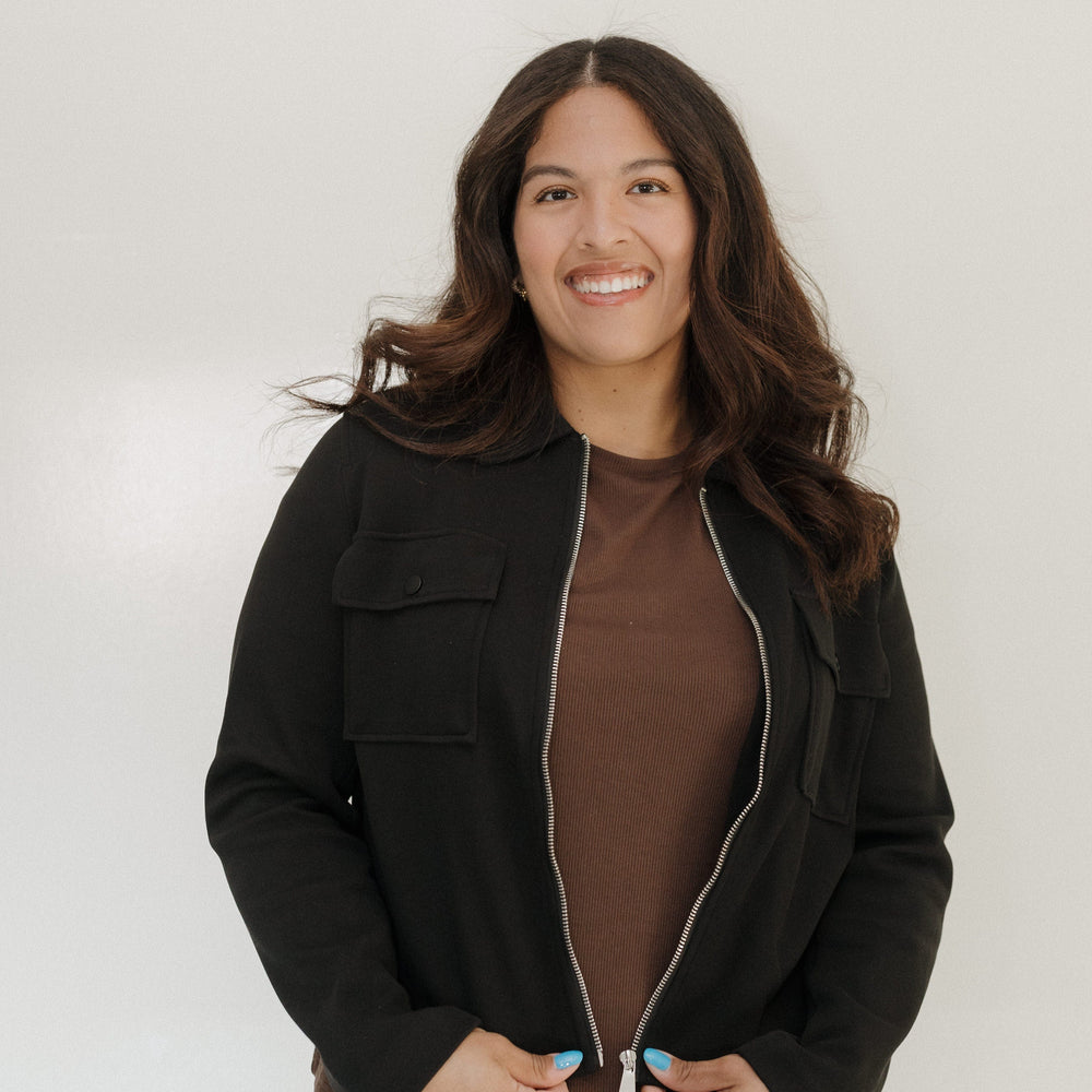 Woman wearing a black jacket over a brown top against a white background