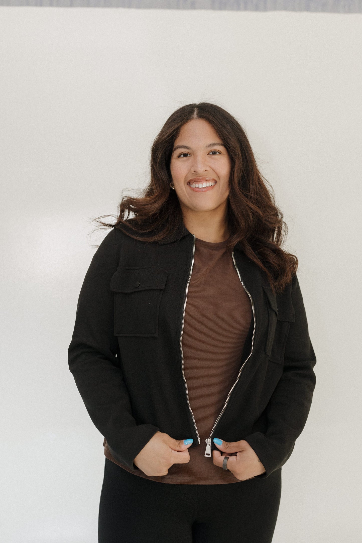 Woman wearing a black jacket over a brown top against a white background