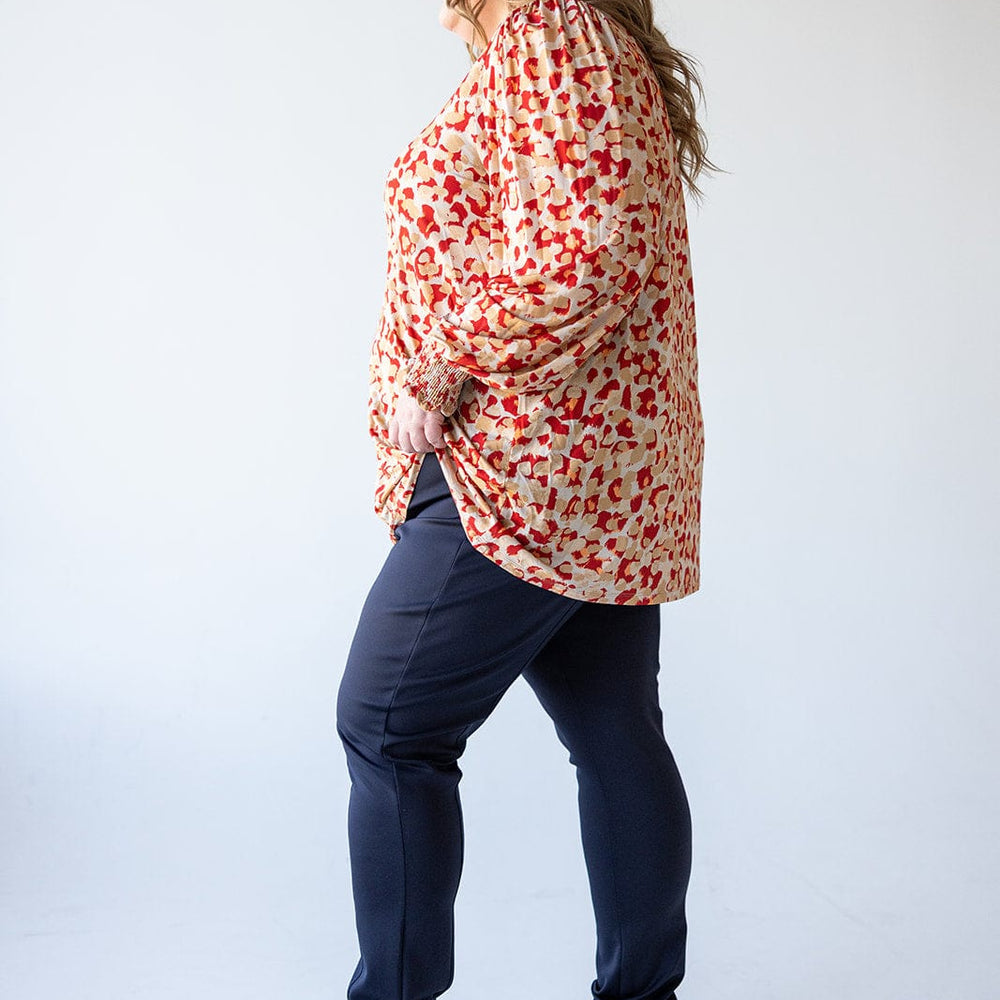 A person in a red patterned blouse and navy slim-straight-leg pants, made of luxurious sateen fabric, stands against a light background, facing left.