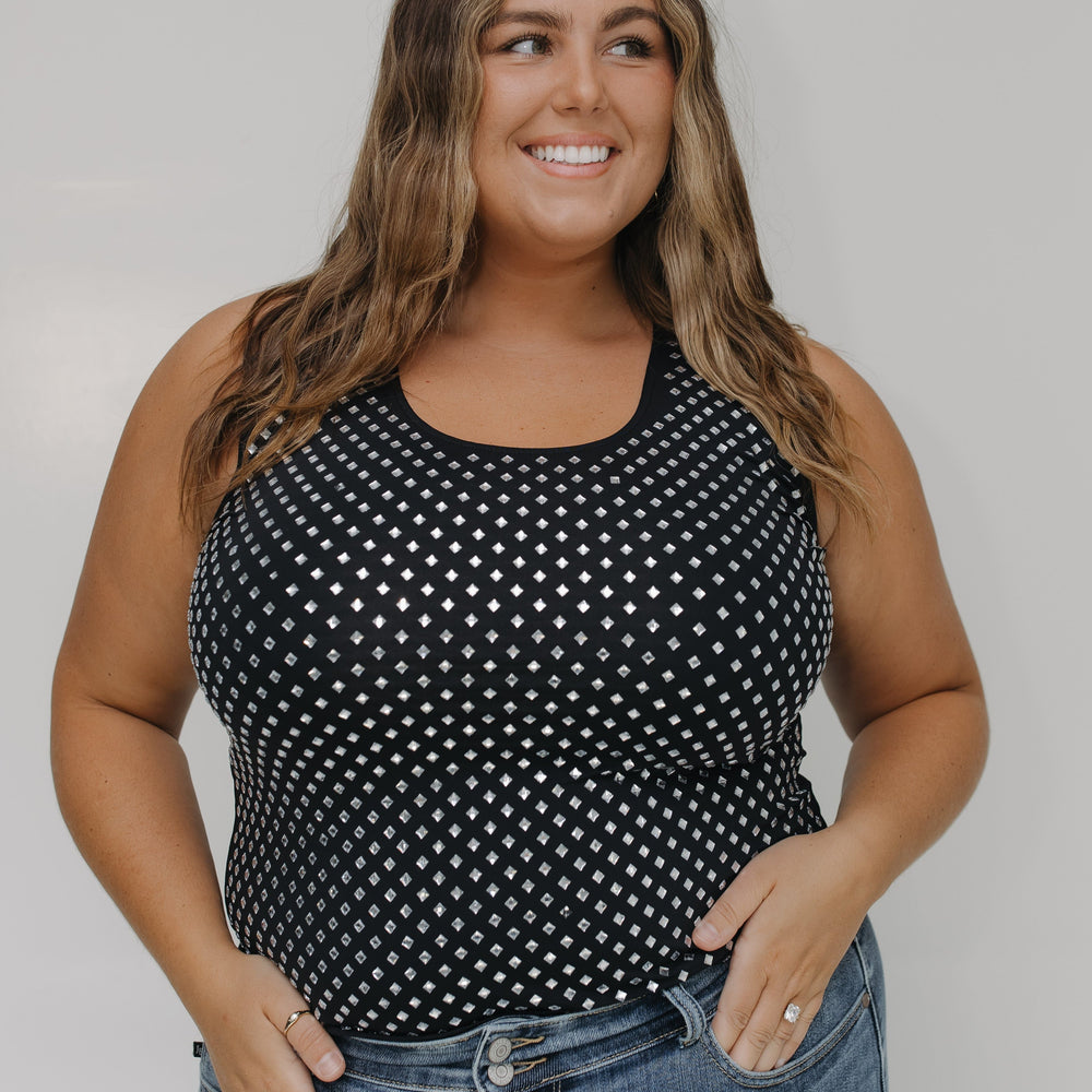 Woman wearing a black tank top with white polka dots and blue jeans against a plain background