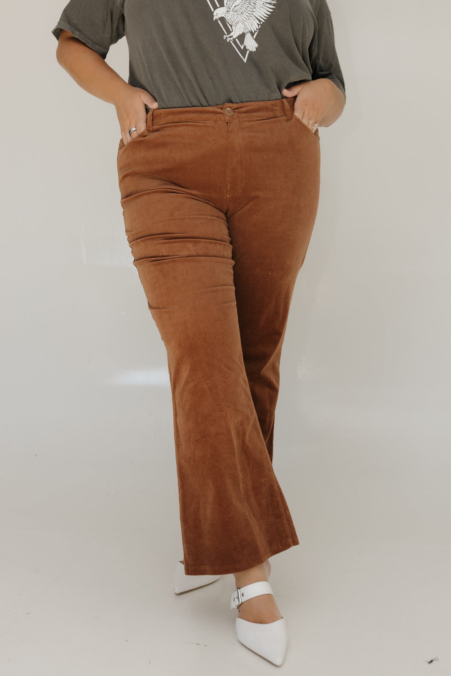 Person wearing brown flared pants and a gray t-shirt with a white graphic on a plain background