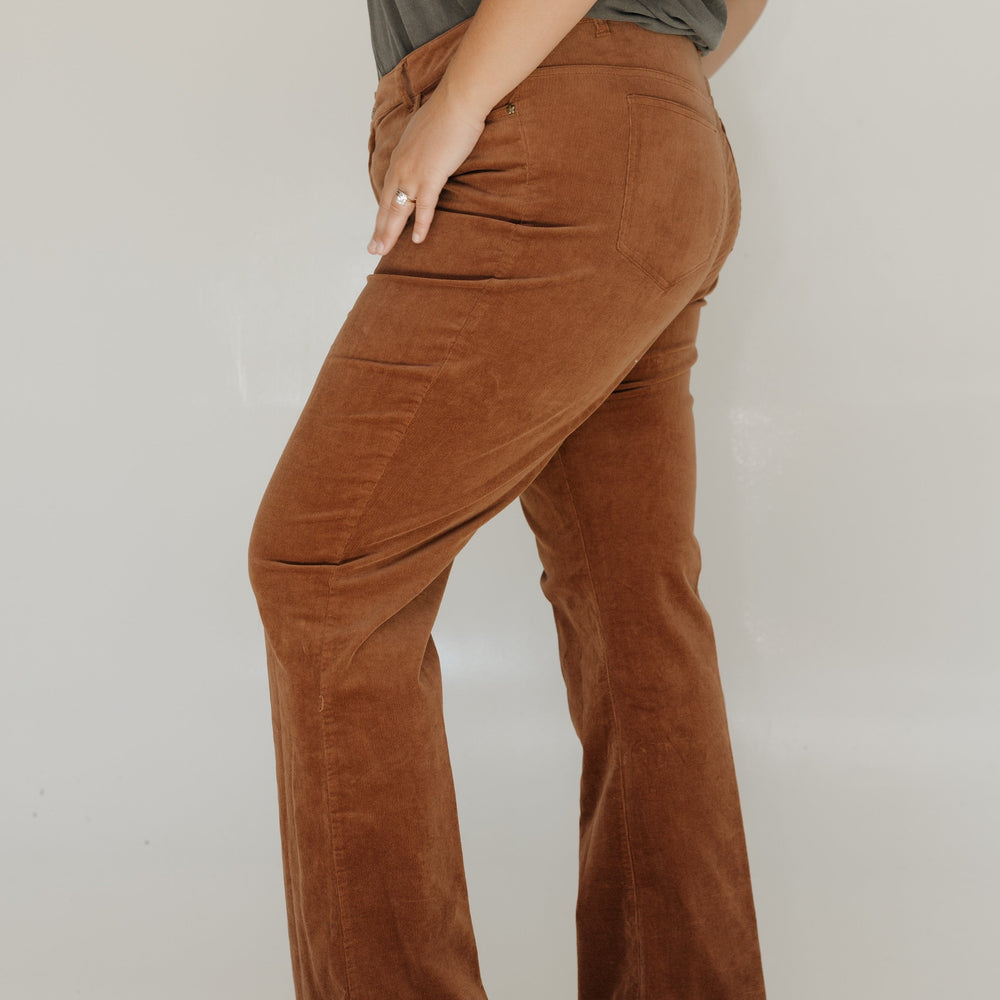 Person wearing brown corduroy pants and a green top on a plain background