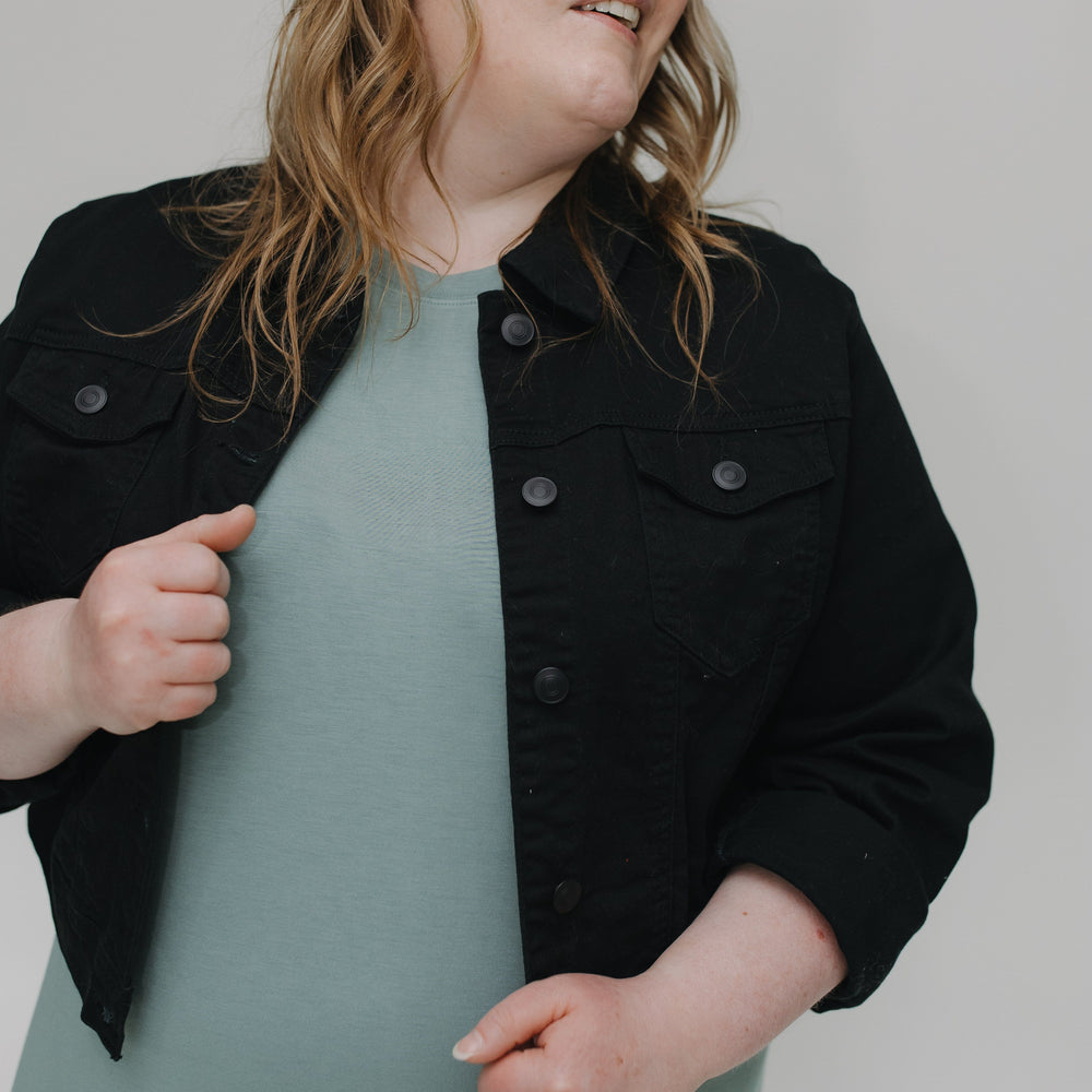 Person wearing a black jacket over a light green dress against a plain background