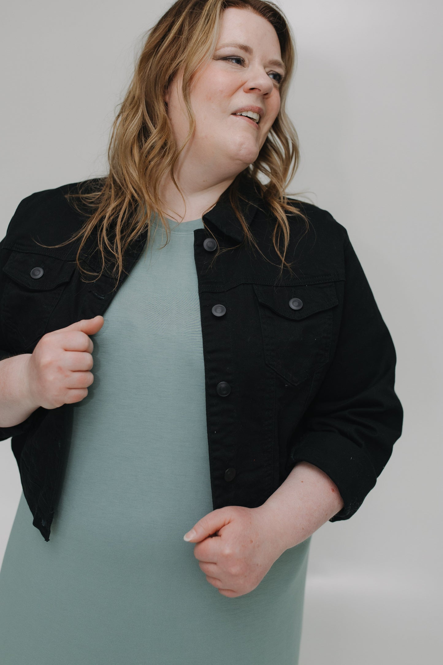 Person wearing a black jacket over a light green dress against a plain background