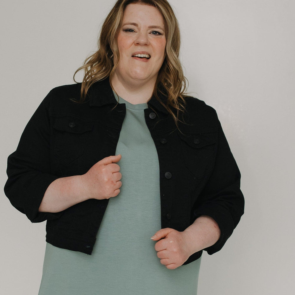 Woman wearing a black jacket over a long light green dress on a white background