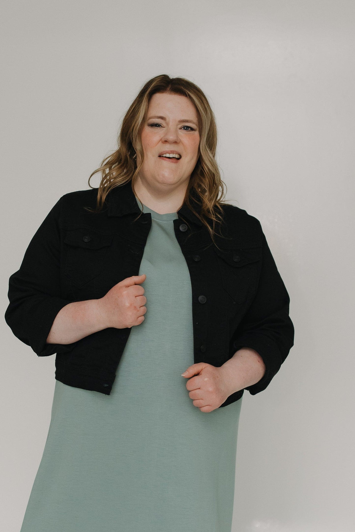 Woman wearing a black jacket over a long light green dress on a white background