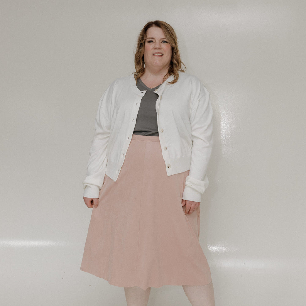 Person wearing a white jacket, gray top, and pink skirt on a white background