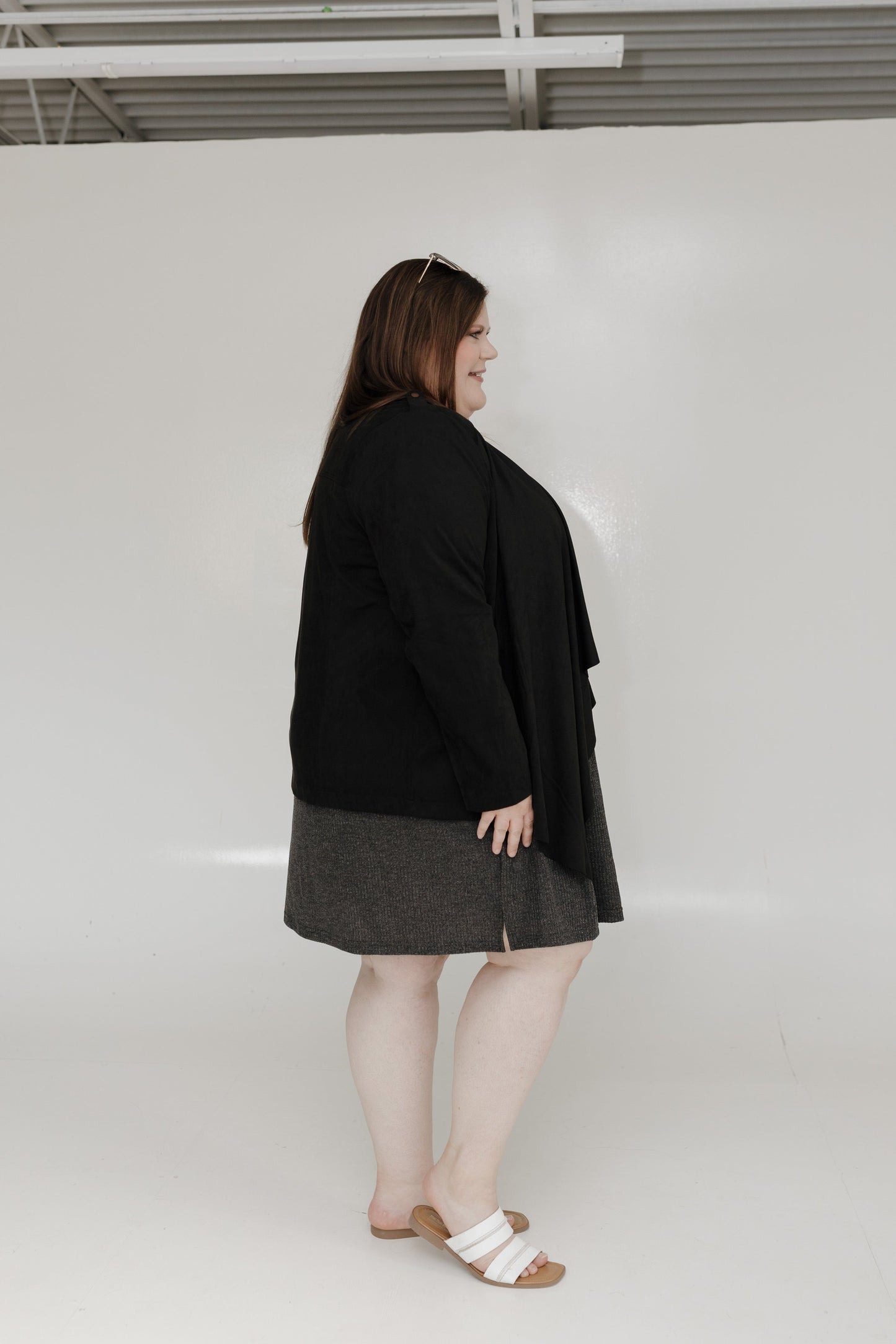 Person wearing a black coat and gray skirt against a white background