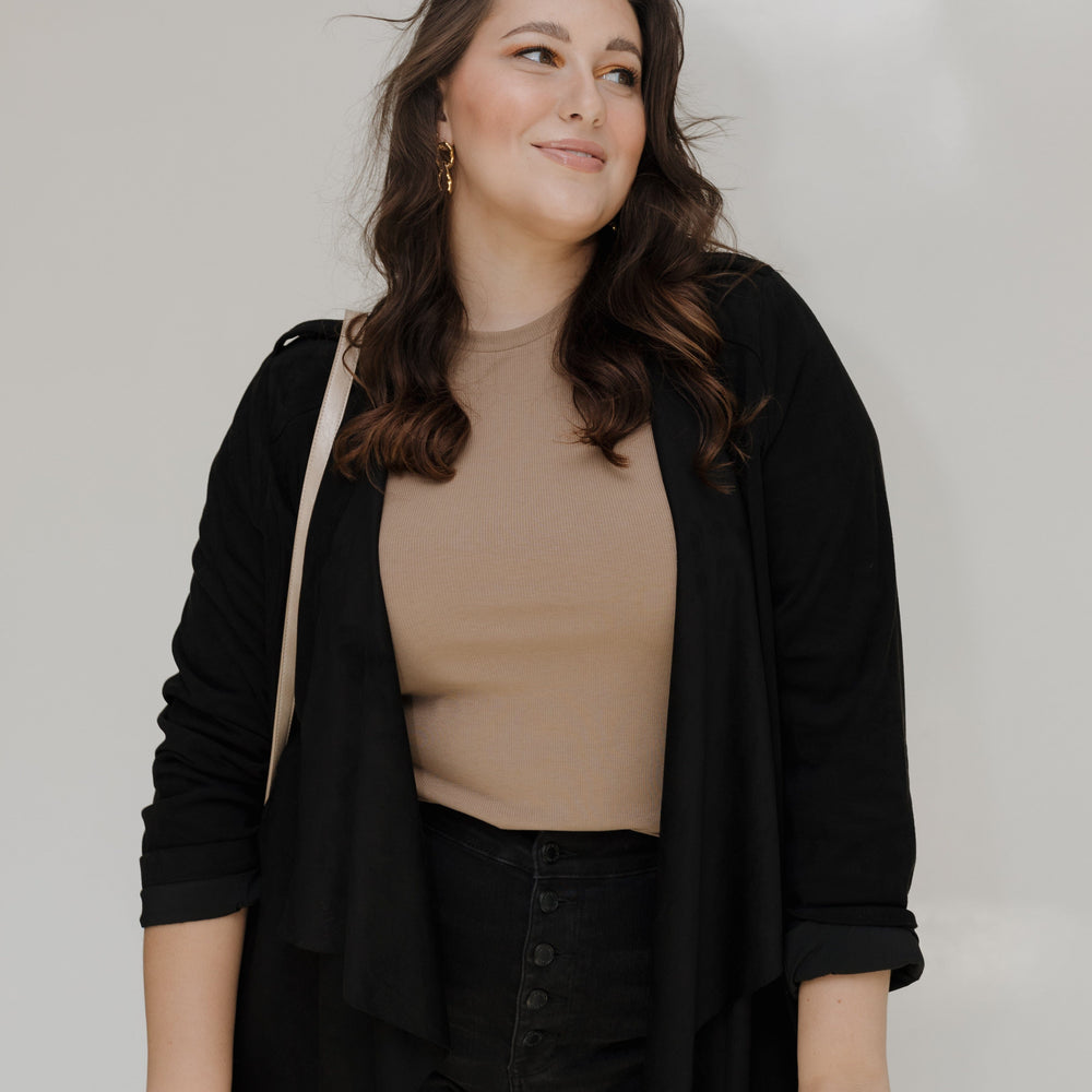 Woman wearing a black cardigan over a beige top and black pants against a white background