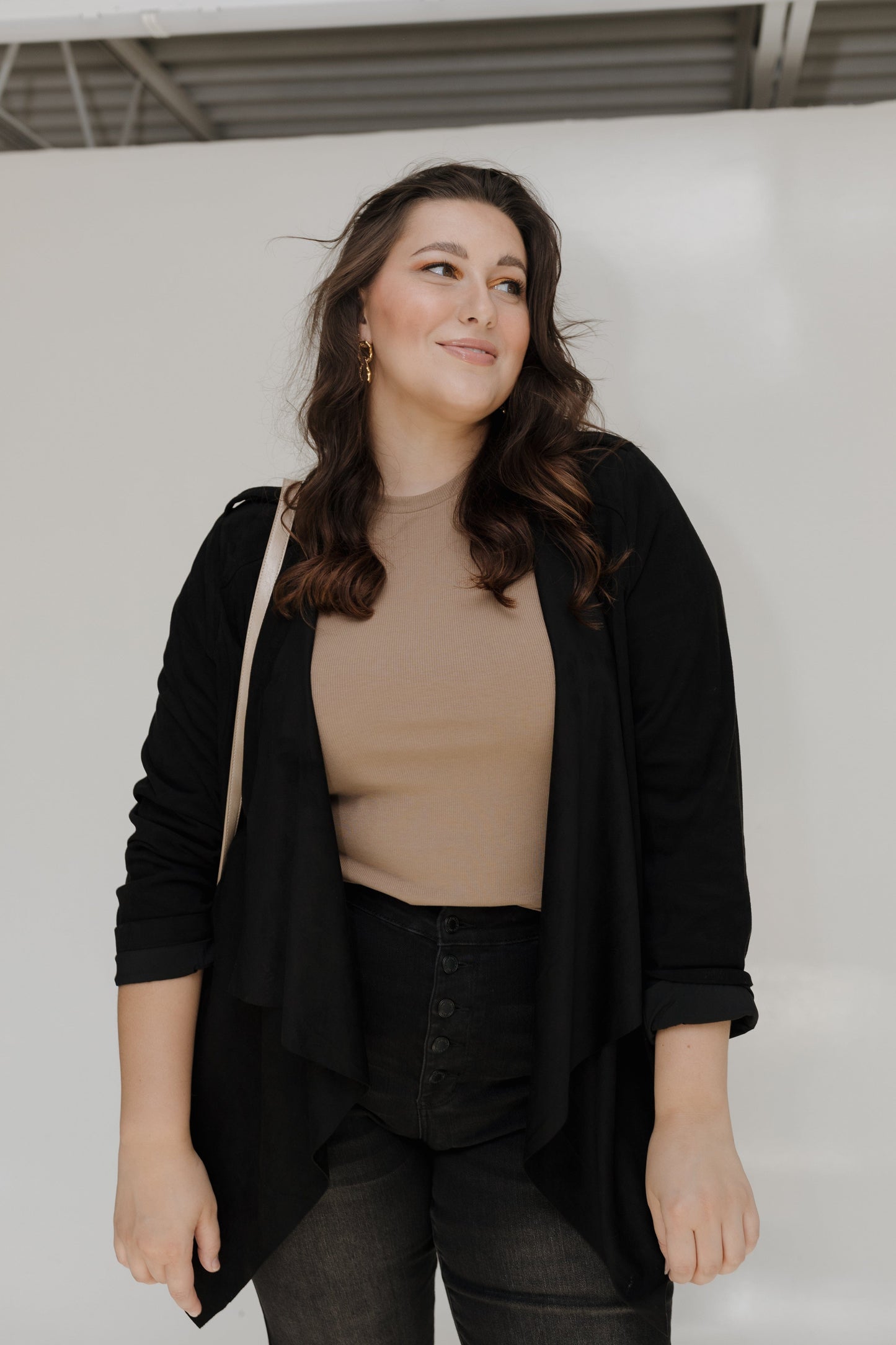 Woman wearing a black cardigan over a beige top and black pants against a white background