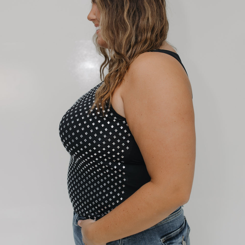 Woman wearing a black tank top with white polka dots and blue jeans against a plain background
