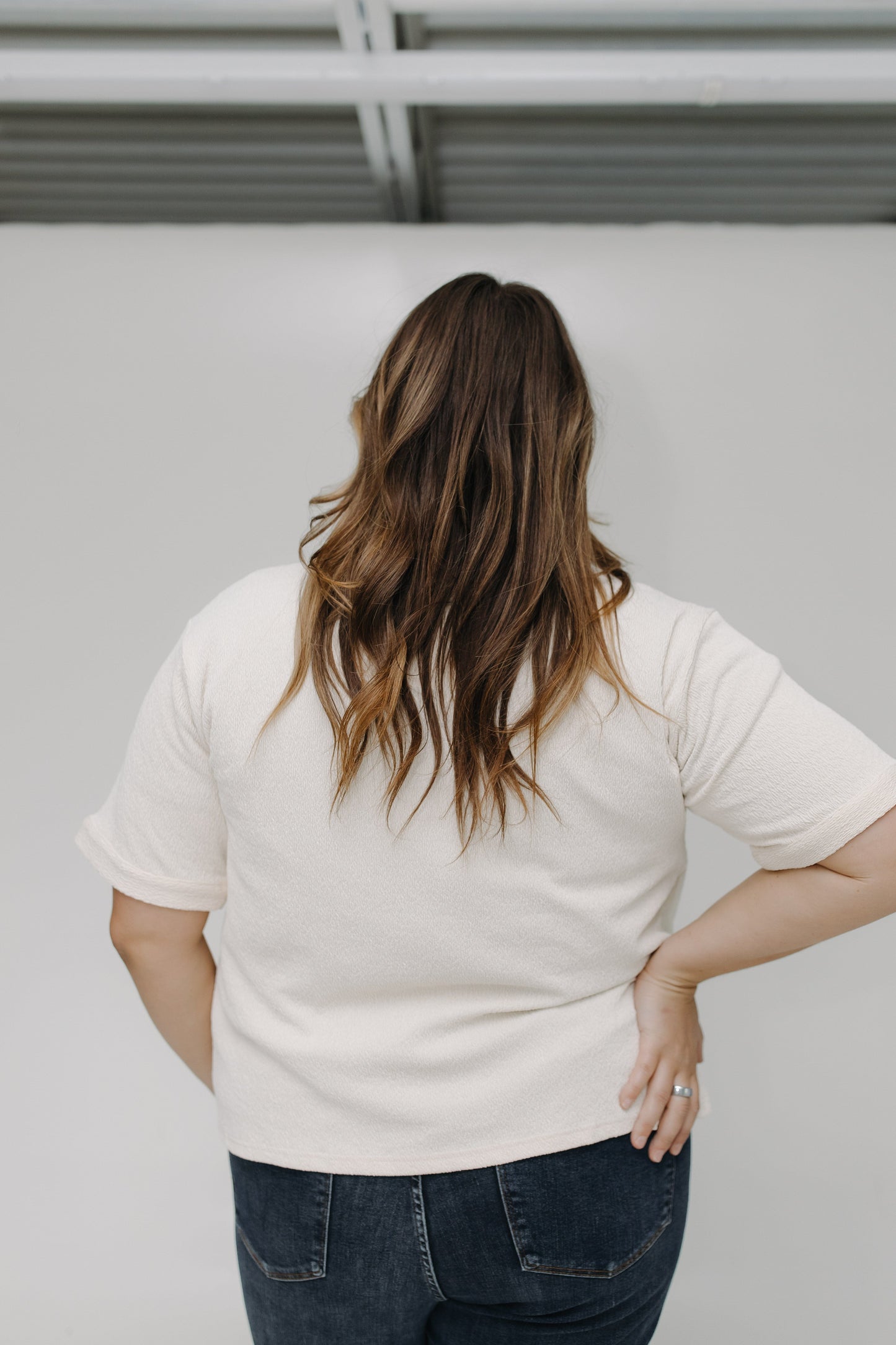 Person wearing a white t-shirt and dark jeans against a plain background