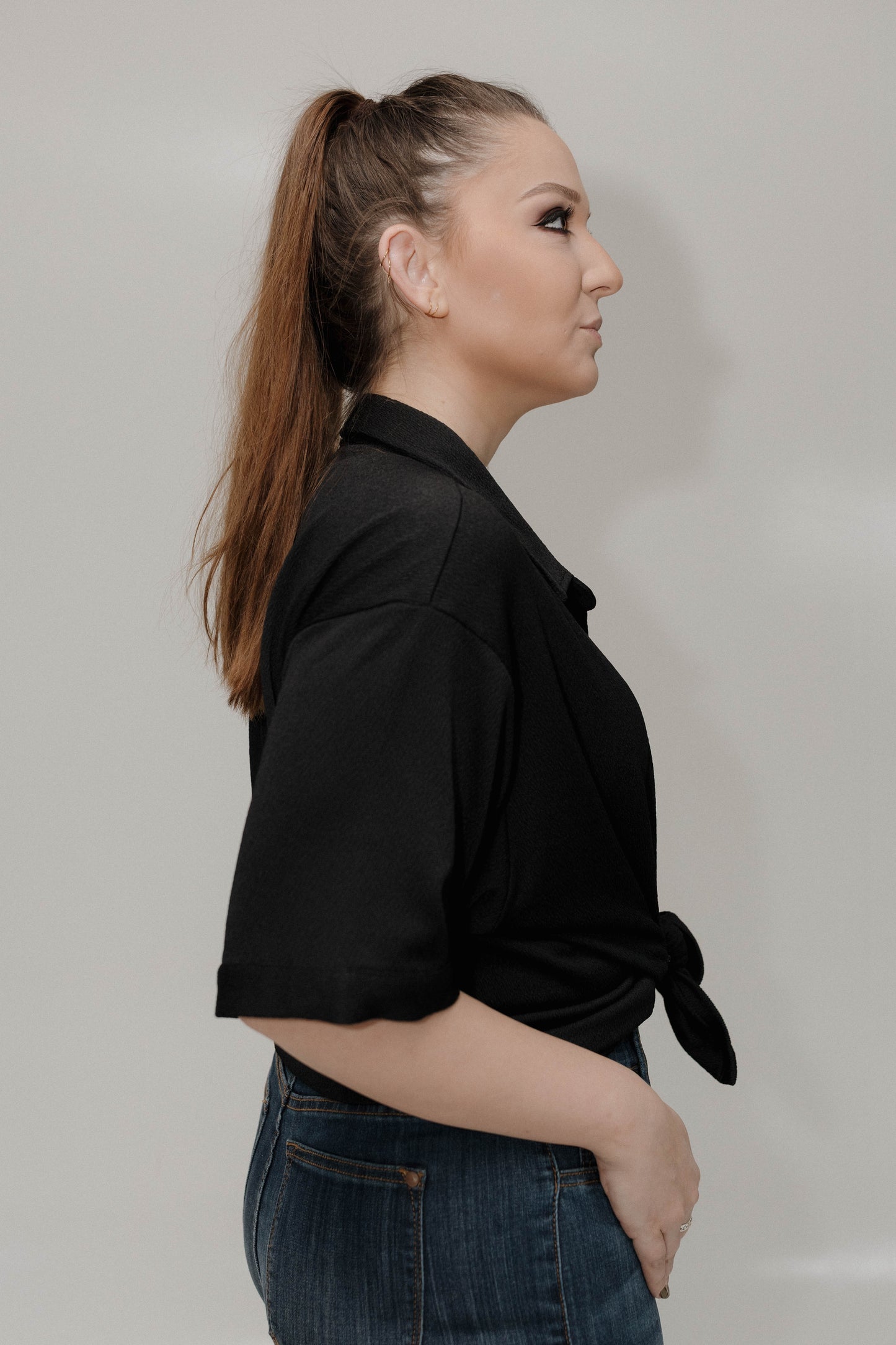 Woman wearing a black shirt and blue jeans against a plain background