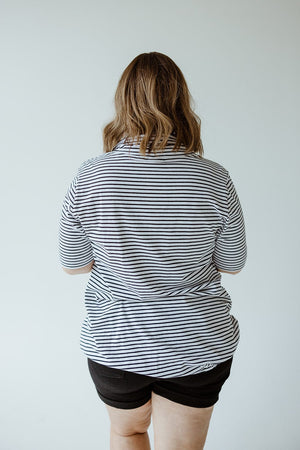 A person with shoulder-length hair, wearing a black and white striped STRIPED COWL NECK SHORT SLEEVE TUNIC IN OFF-WHITE by Love Marlow and black shorts, is standing with their back to the camera against a plain background.