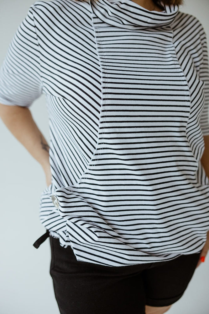 Person wearing a Love Marlow STRIPED COWL NECK SHORT SLEEVE TUNIC IN OFF-WHITE and black pants, standing with one hand on their hip.