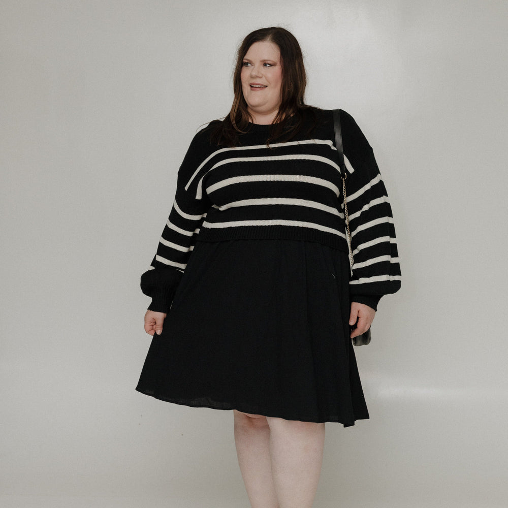 Person wearing a black and white striped sweater with a black skirt on a white background