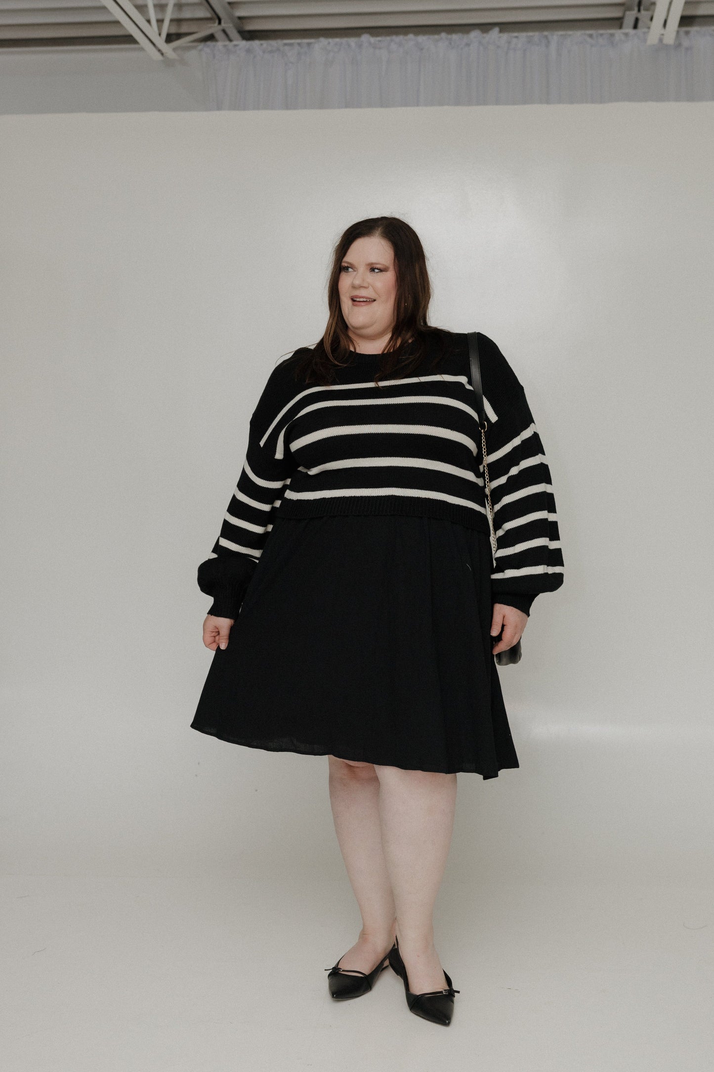 Person wearing a black and white striped sweater with a black skirt on a white background