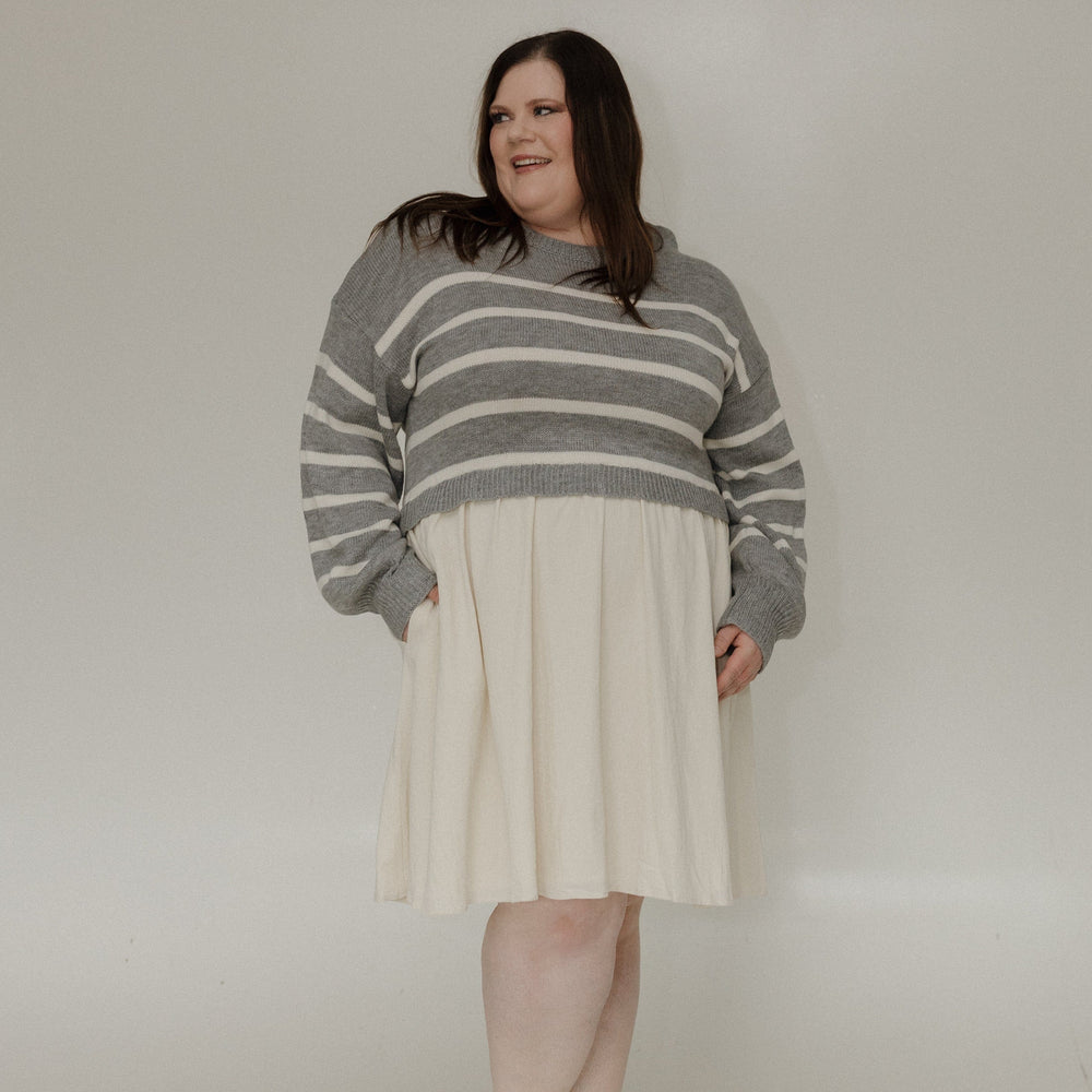 Person wearing a gray and white striped sweater over a cream dress on a plain background