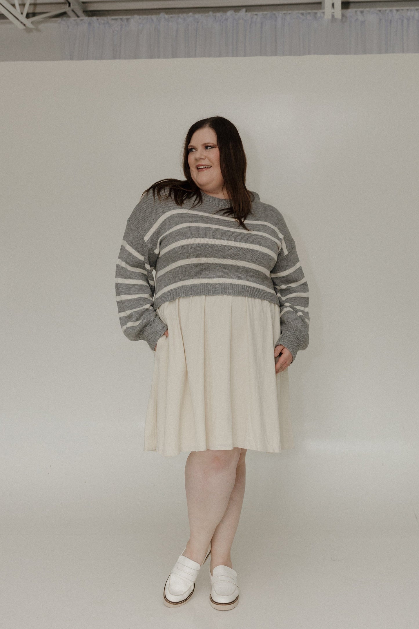 Person wearing a gray and white striped sweater over a cream dress on a plain background
