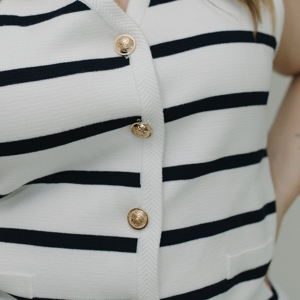 Close-up of a white cardigan with black stripes and gold buttons.