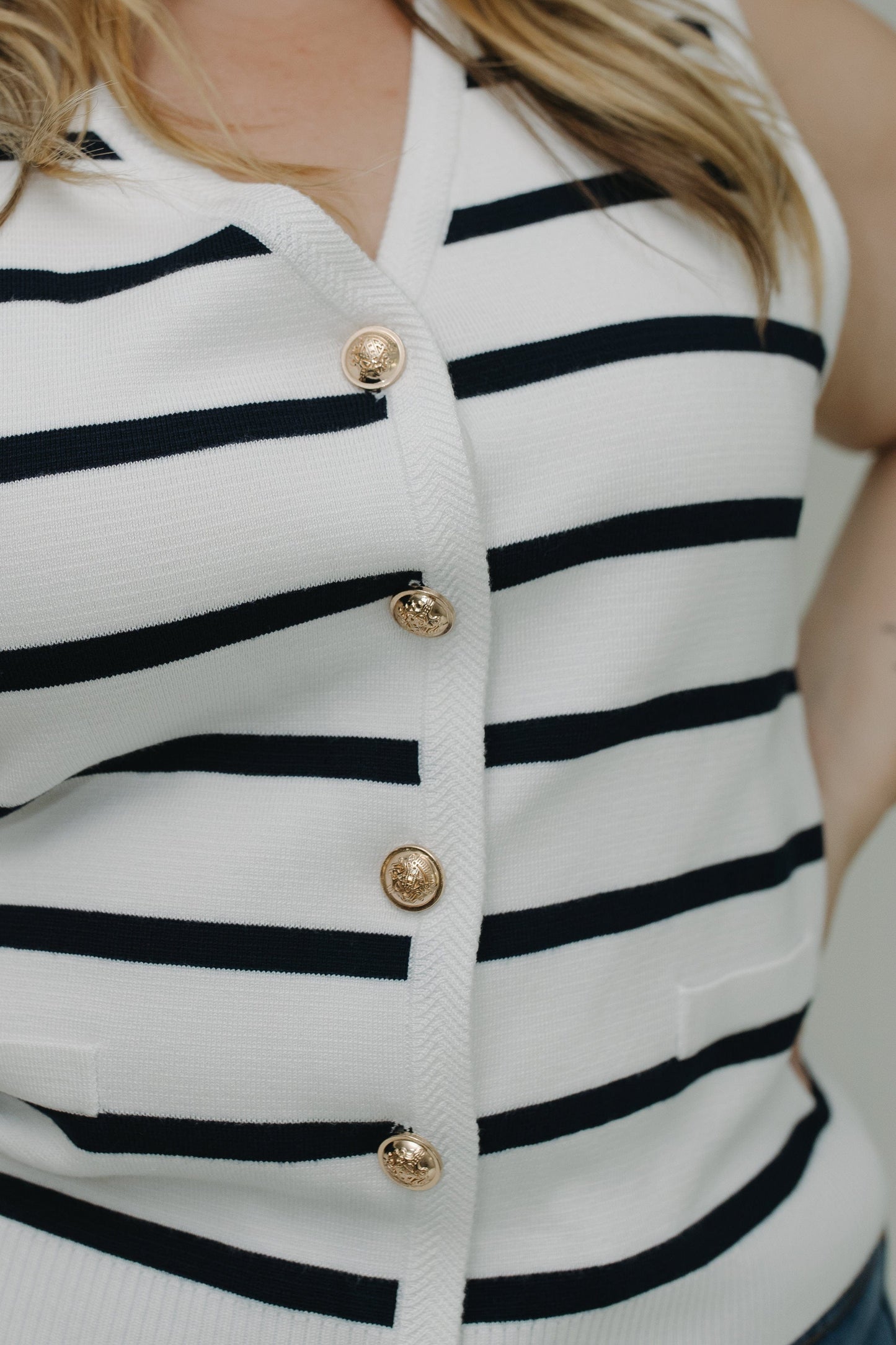 Close-up of a white cardigan with black stripes and gold buttons.