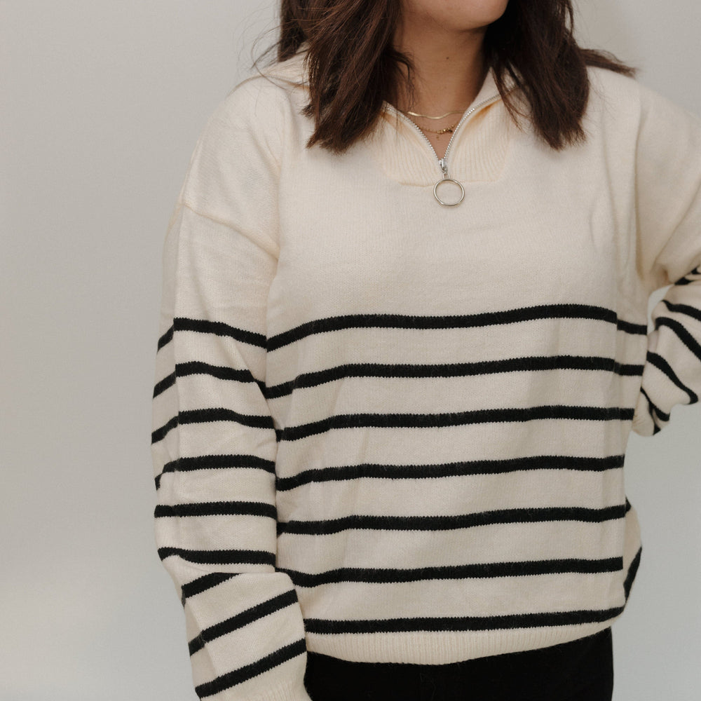 Woman wearing a cream sweater with black stripes against a plain background