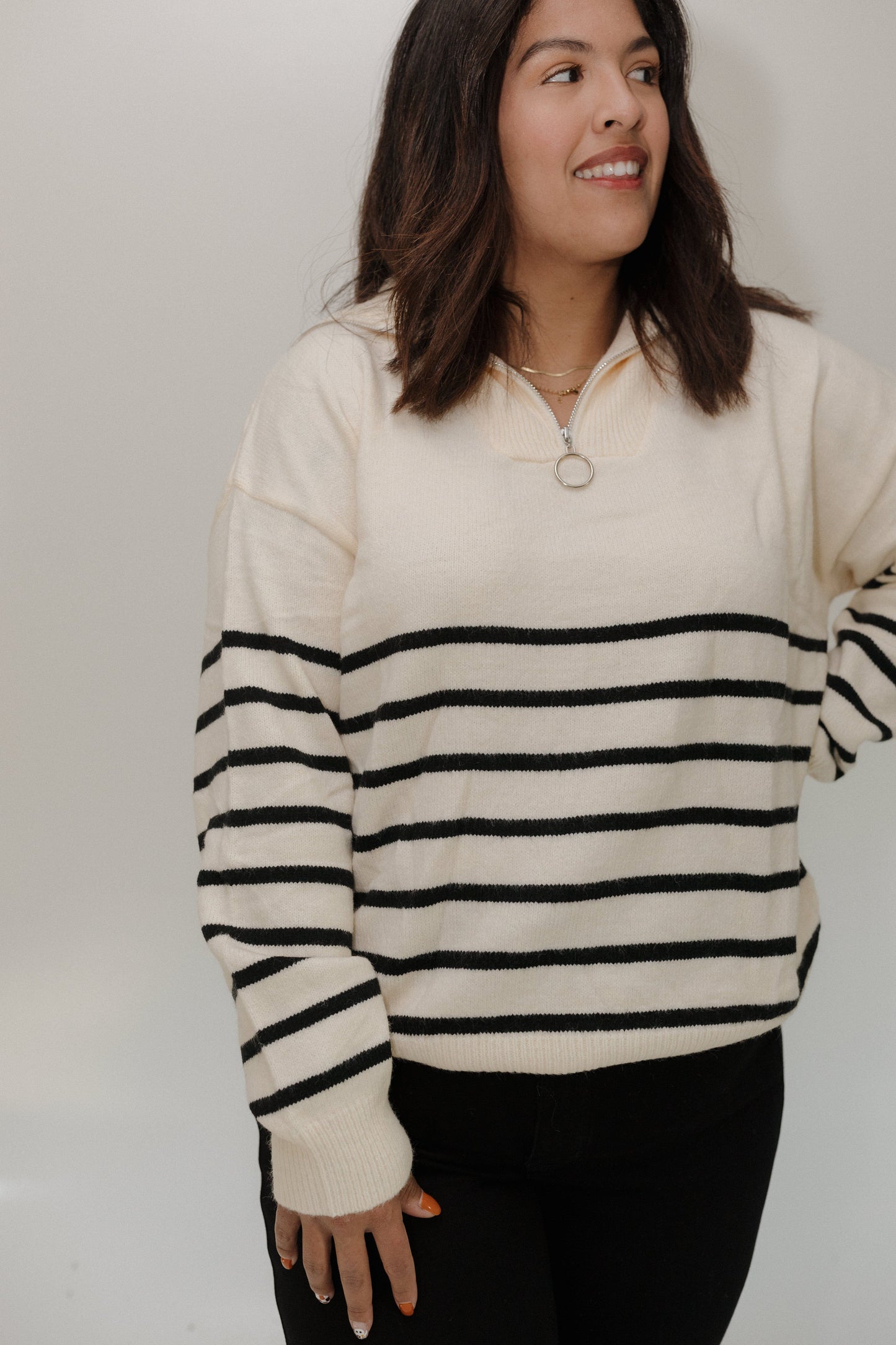 Woman wearing a cream sweater with black stripes against a plain background