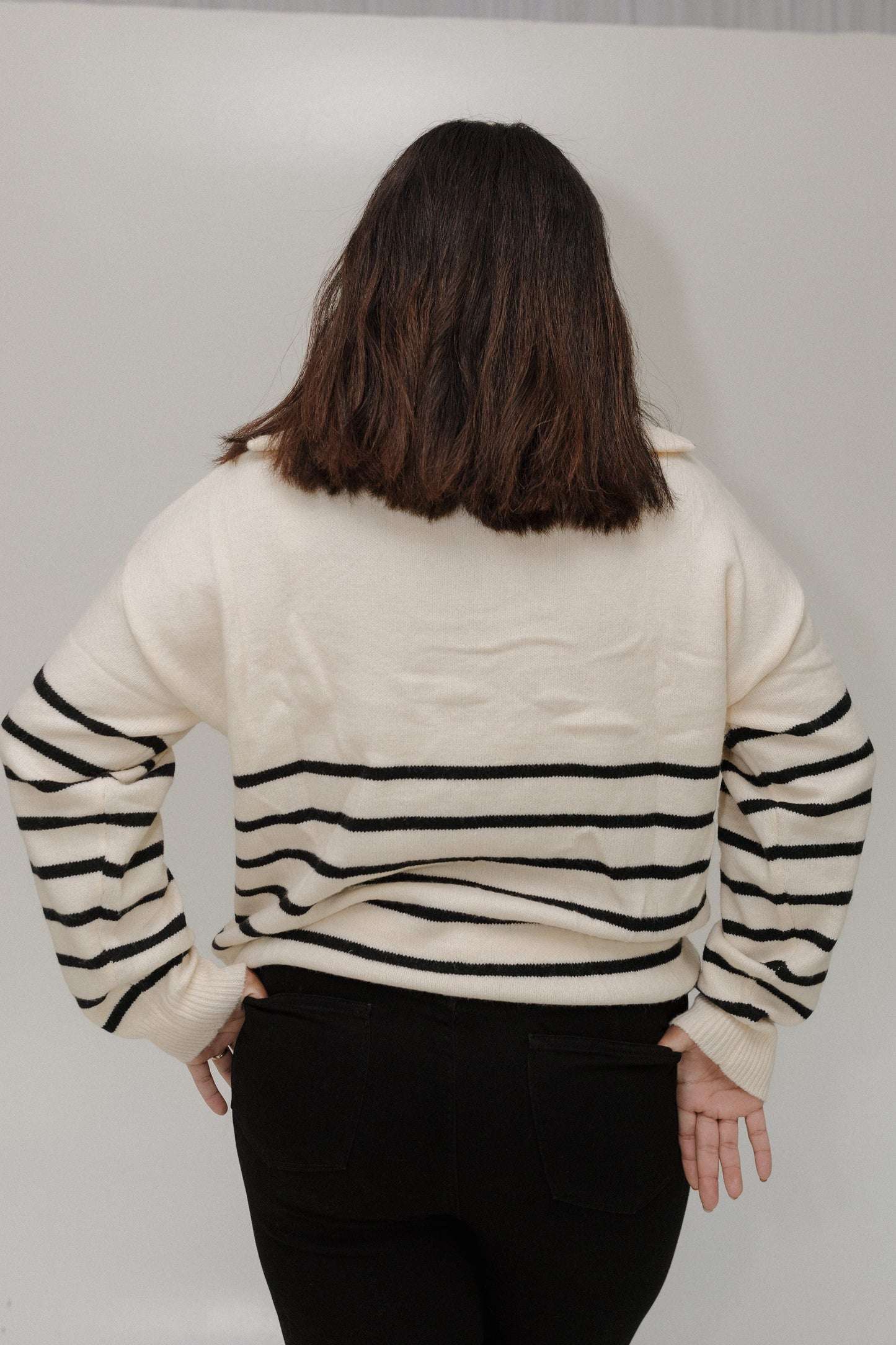 Person wearing a cream sweater with black stripes on a plain background