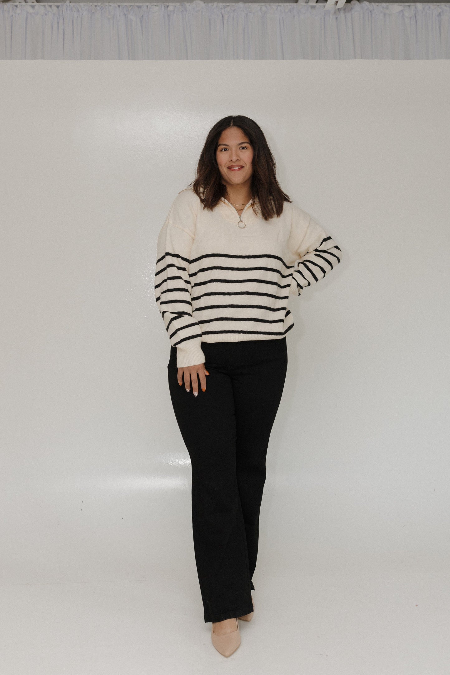 Woman wearing a striped sweater and black pants against a white background