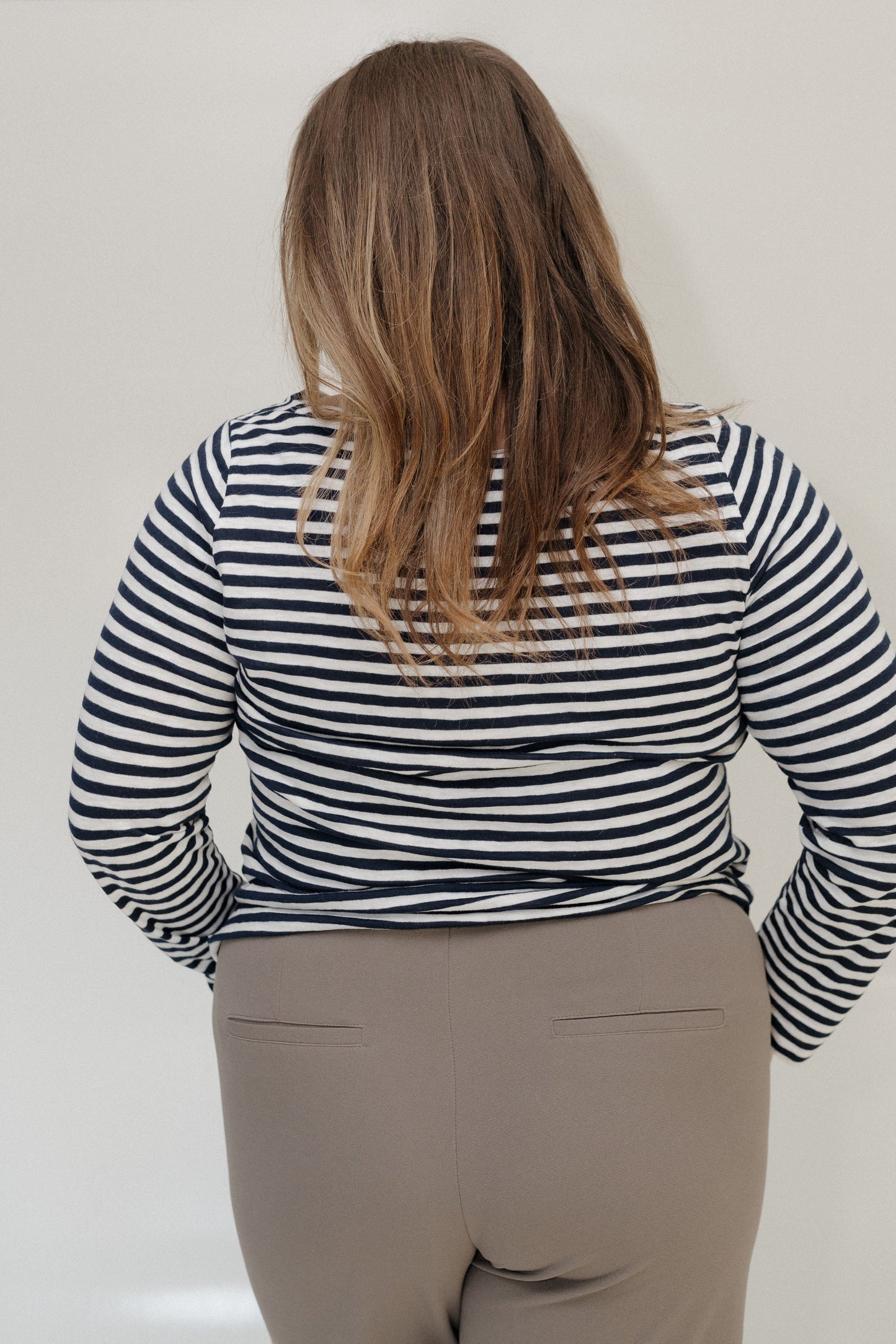 Person wearing a black and white striped shirt and beige pants against a plain background