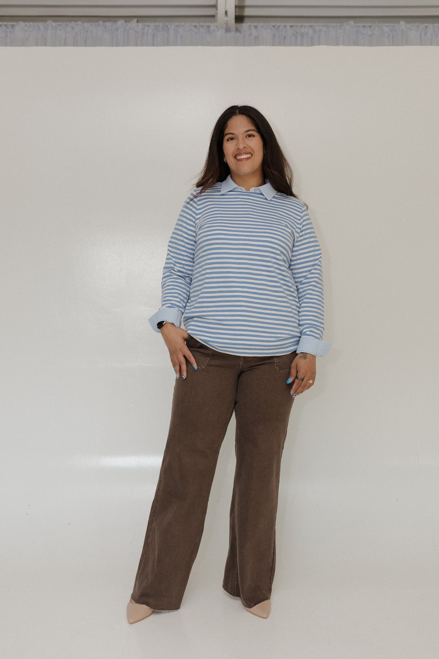 Woman wearing a blue striped shirt and brown pants against a white background