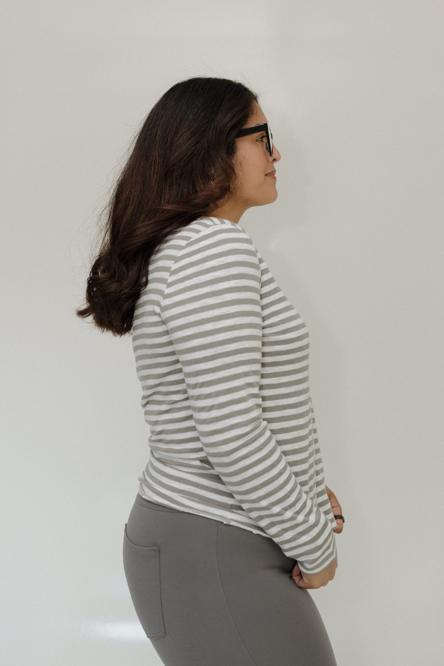 Woman wearing a striped long-sleeve shirt and gray pants against a plain background