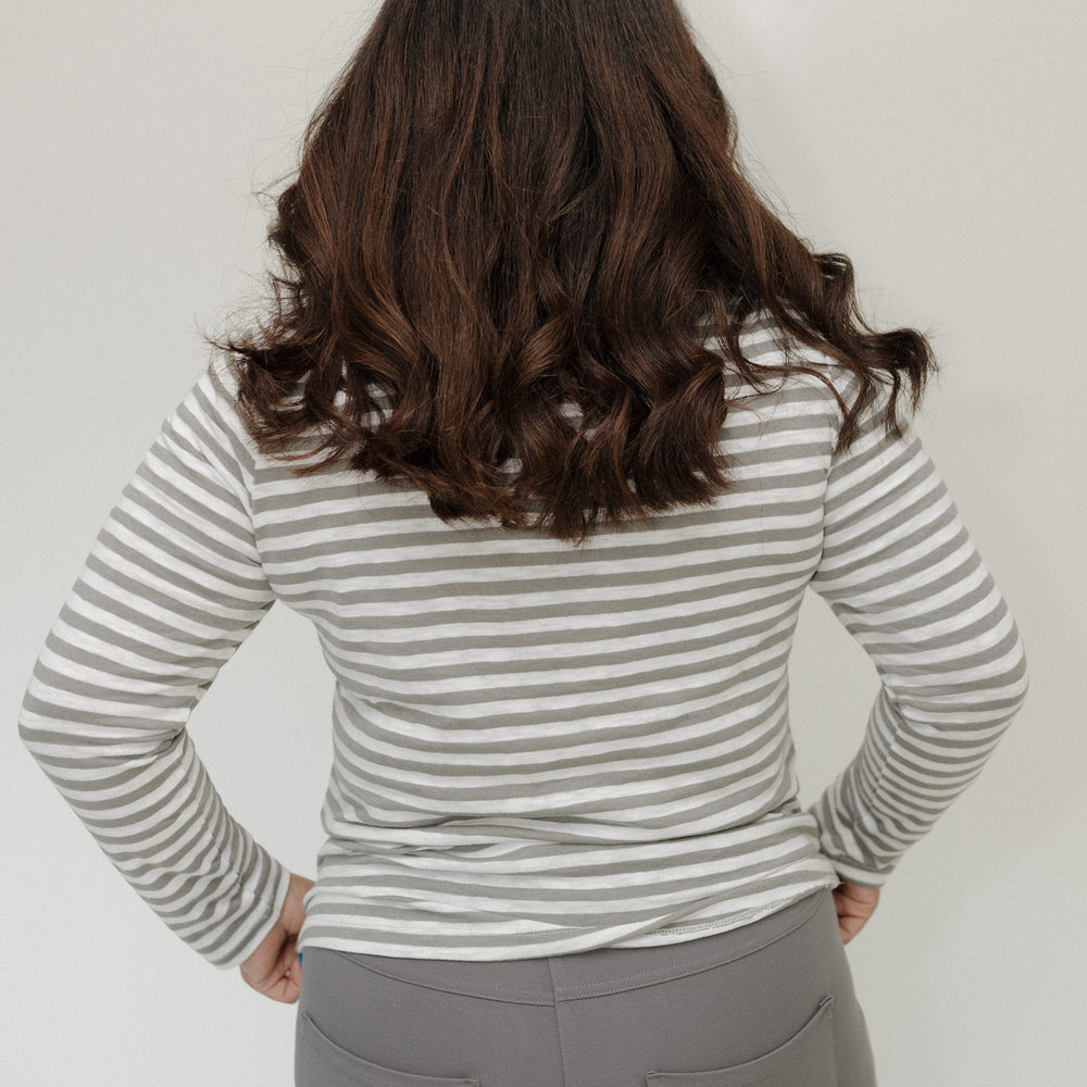 Person wearing a striped long-sleeve shirt and gray pants against a plain background
