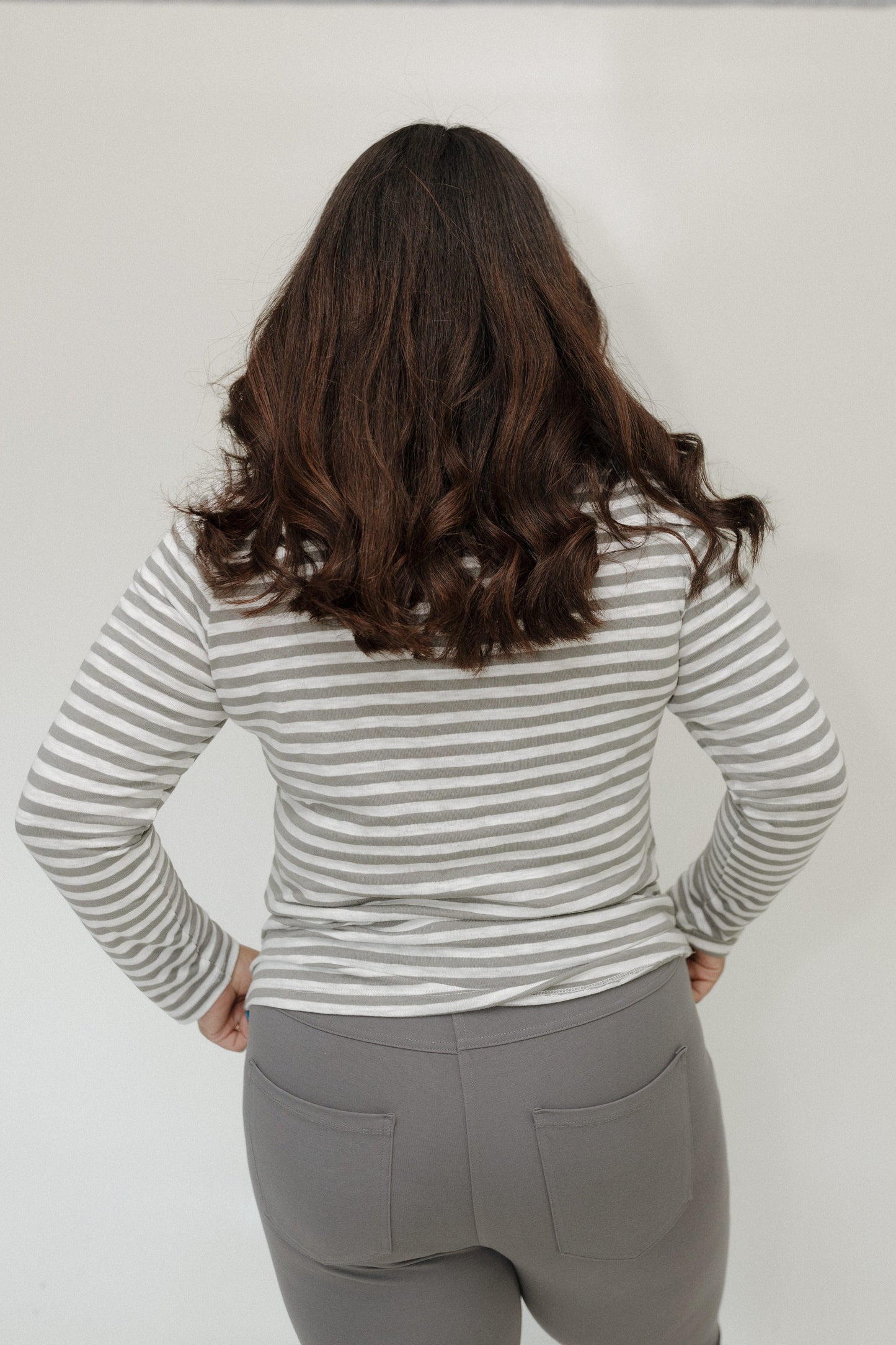 Person wearing a striped long-sleeve shirt and gray pants against a plain background