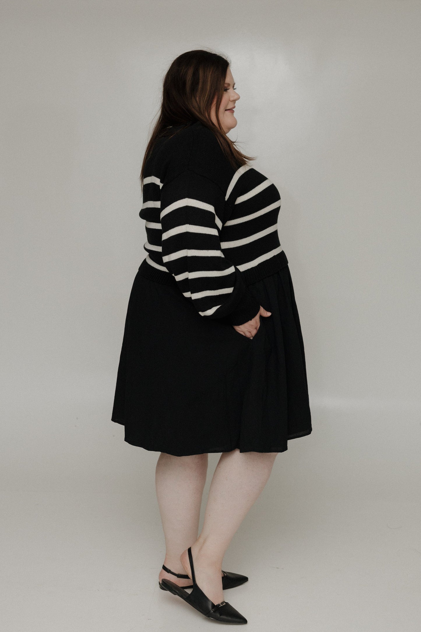 Person wearing a black and white striped sweater with a black skirt on a plain background