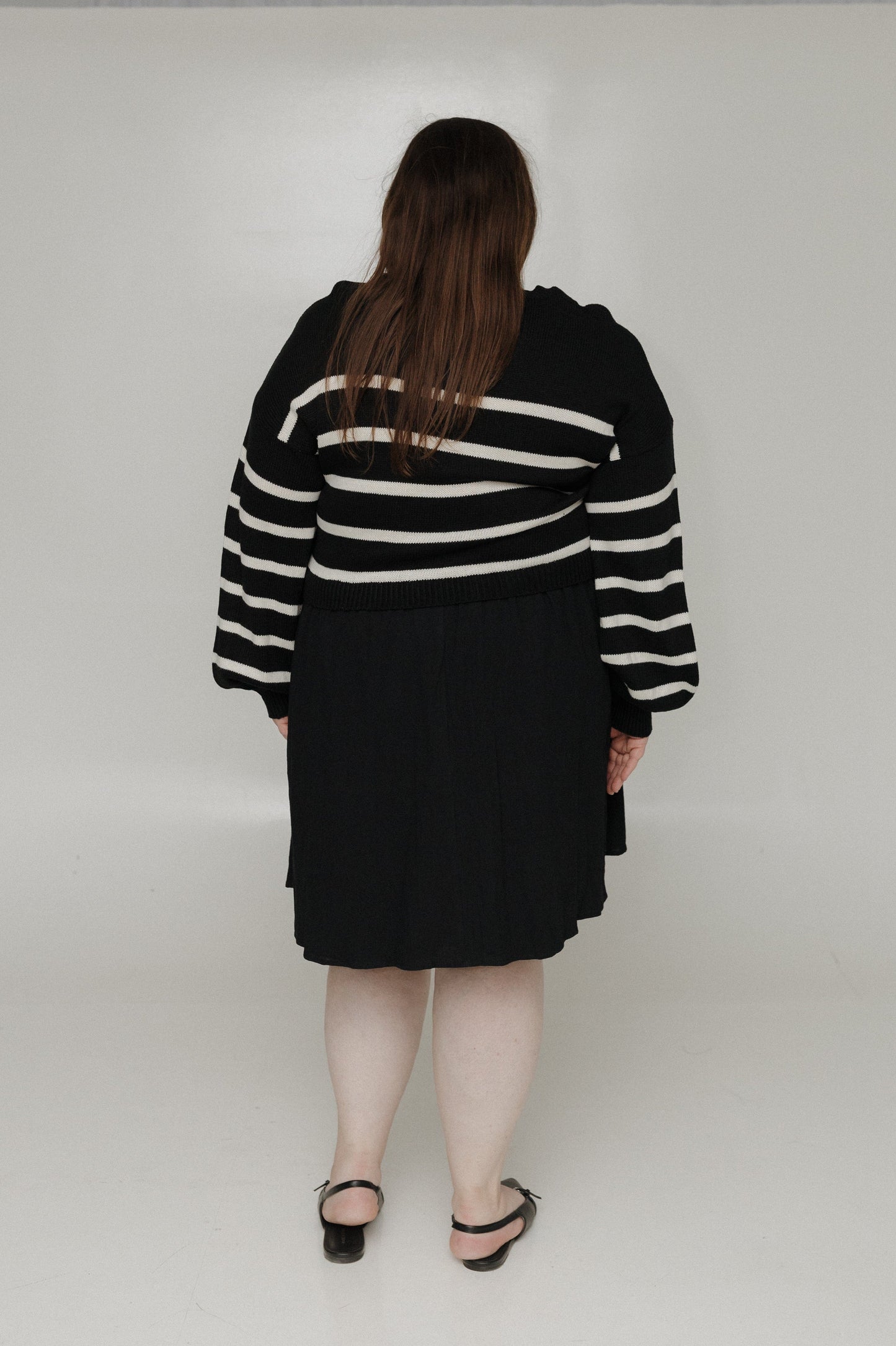 Person wearing a black and white striped sweater and skirt on a plain background