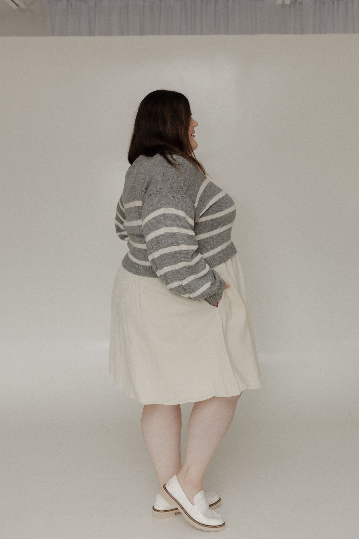 Person wearing a gray and white striped sweater with a beige skirt on a plain background
