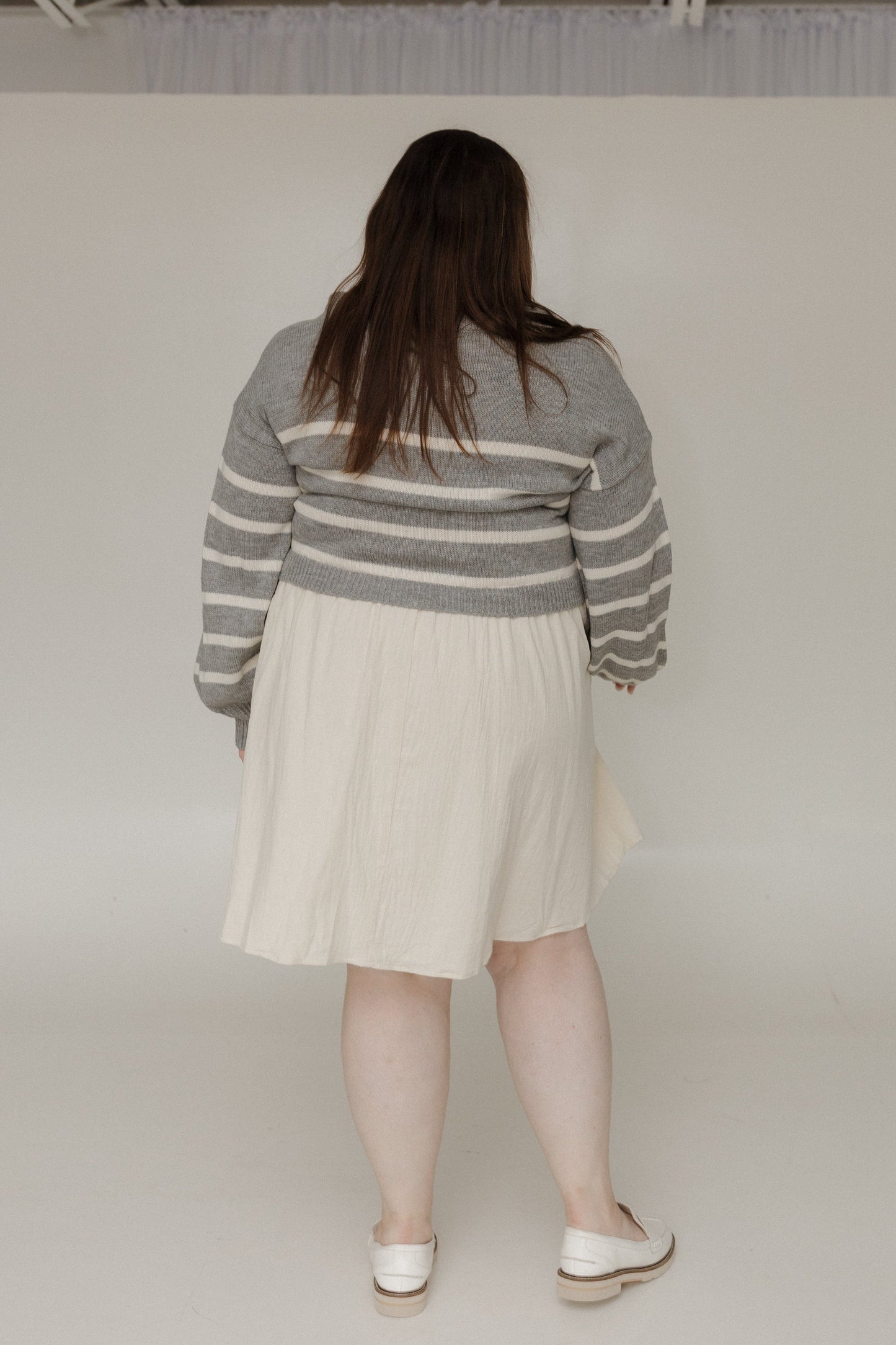 Person wearing a gray and white striped sweater and beige skirt on a plain background