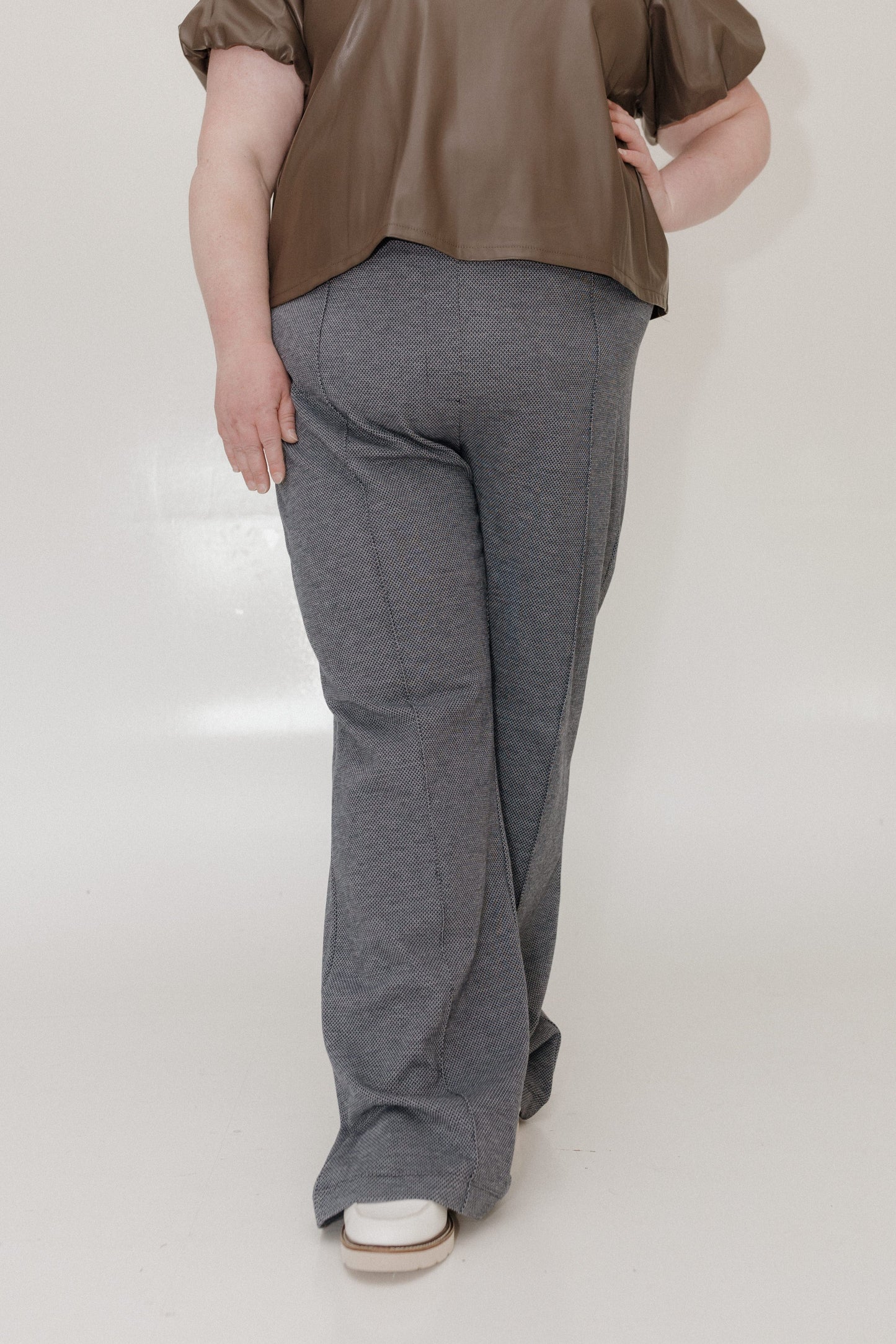 Person wearing a brown top and gray pants on a plain background
