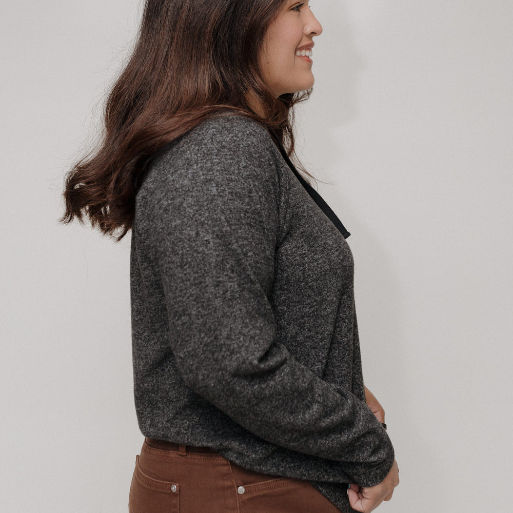 Woman wearing a gray sweater and brown pants against a plain background