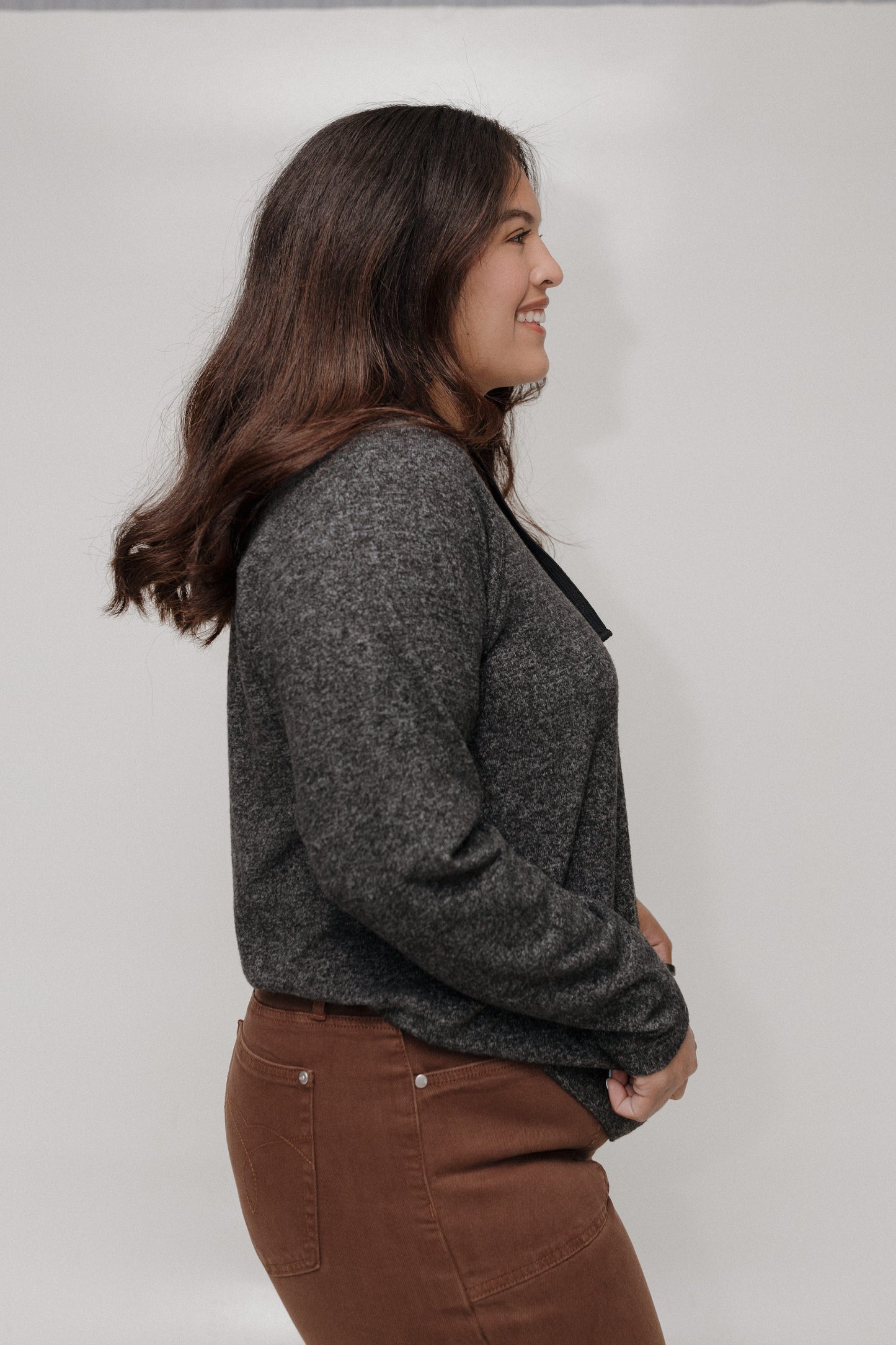 Woman wearing a gray sweater and brown pants against a plain background