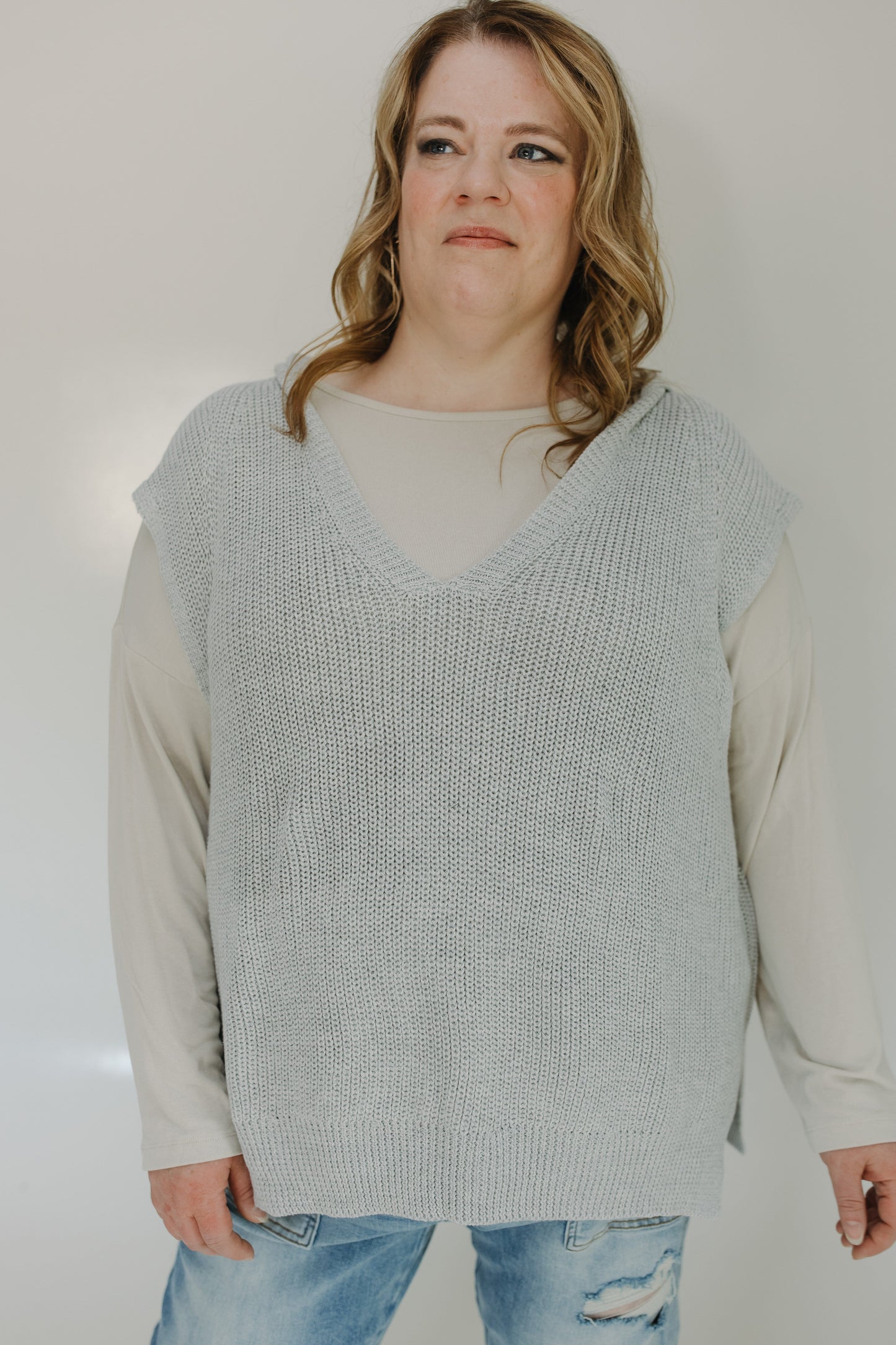 Person wearing a light gray knitted vest over a beige shirt with a plain background