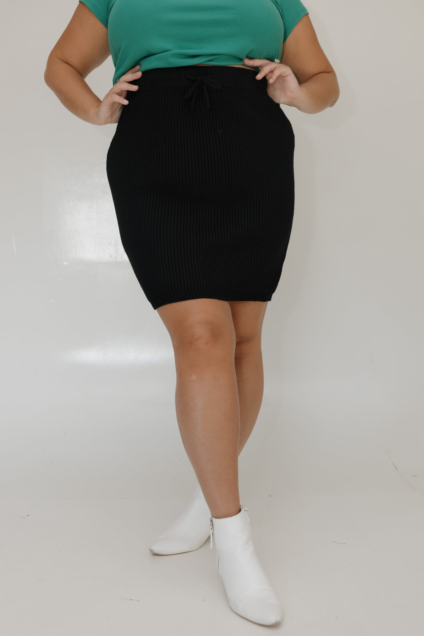 Person wearing a black skirt and green top on a white background