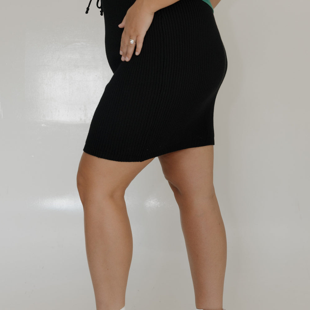 Person wearing a green top, black skirt, and white boots on a plain background