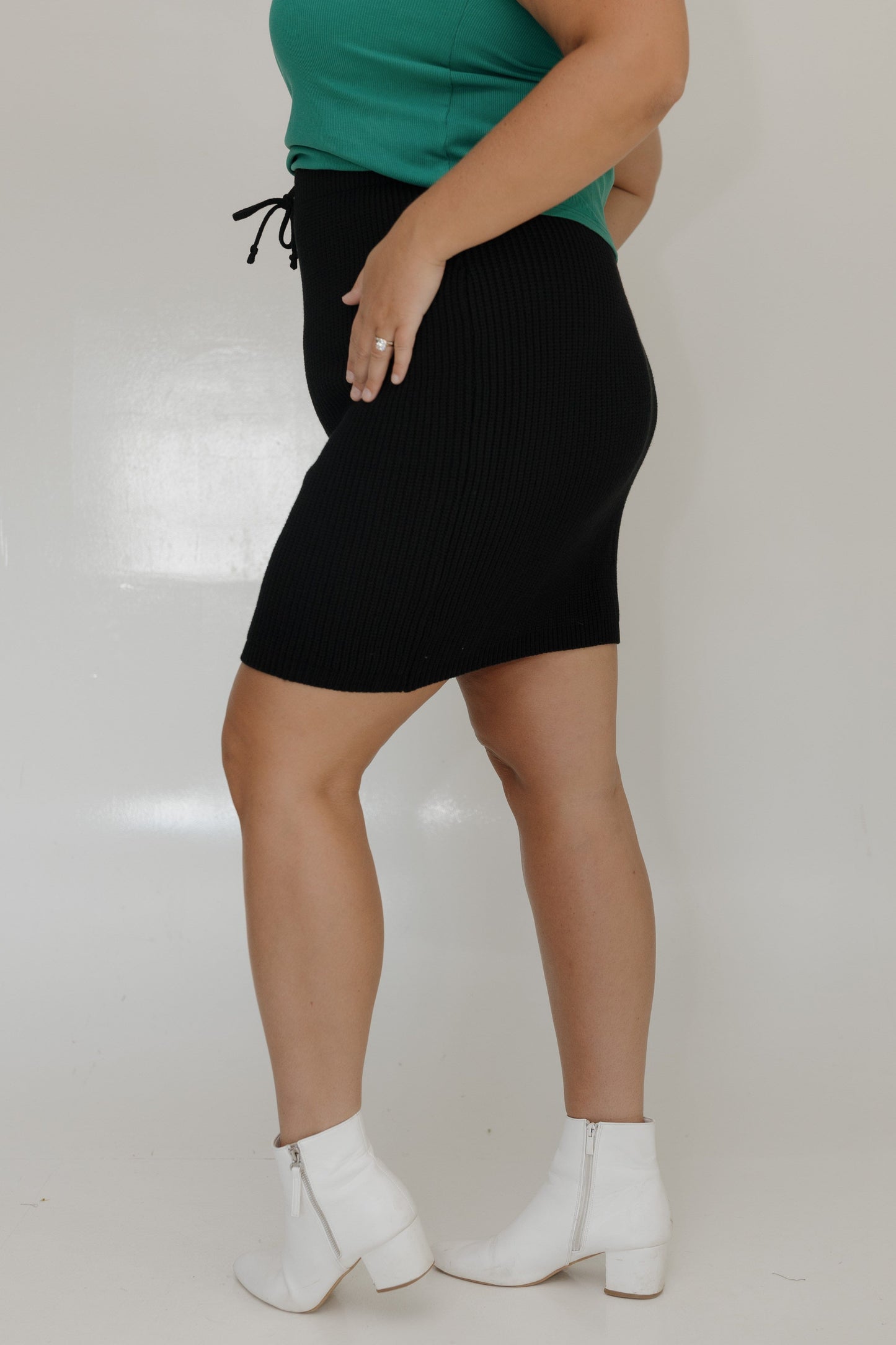 Person wearing a green top, black skirt, and white boots on a plain background