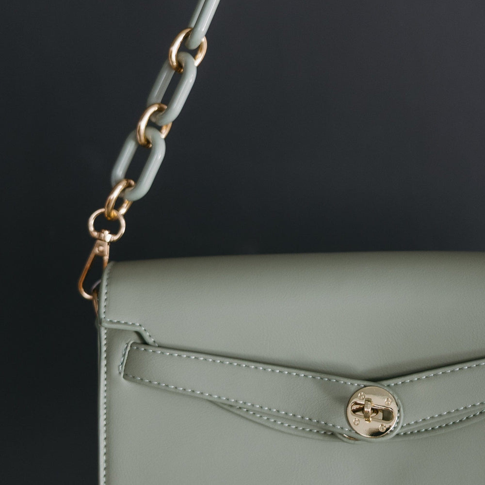 Green handbag with a chain strap held by a hand against a dark background