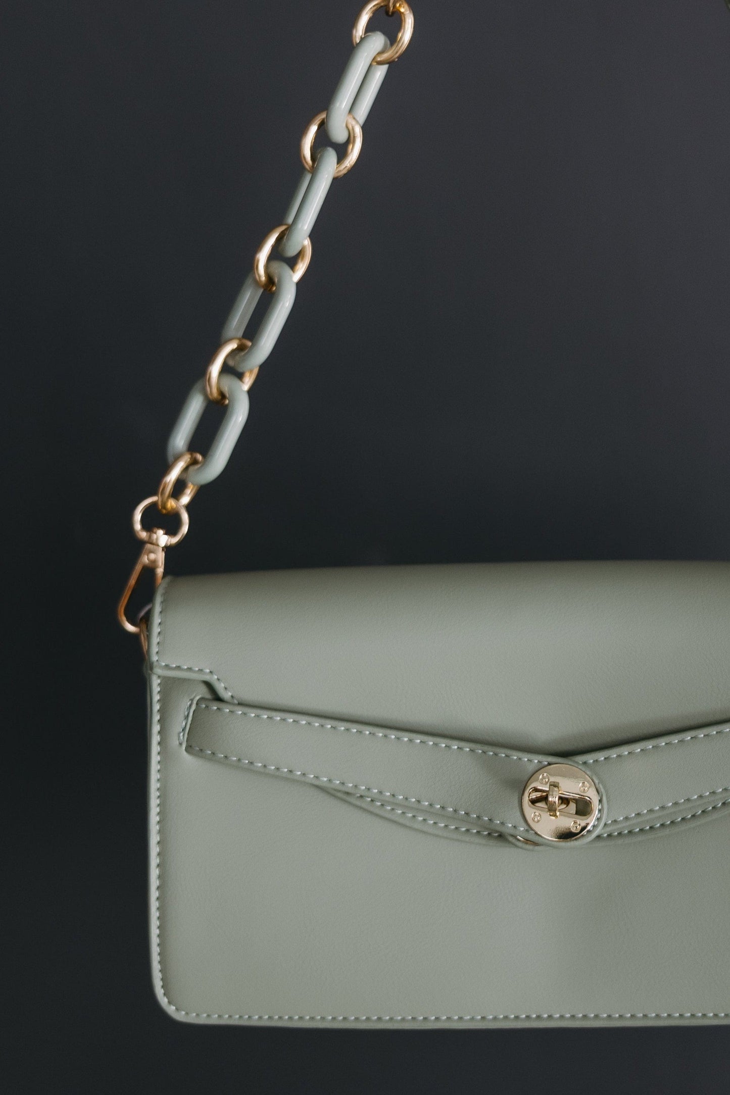 Green handbag with a chain strap held by a hand against a dark background