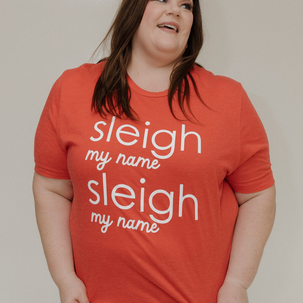 Person wearing a red t-shirt with 'sleigh my name' text on a plain background